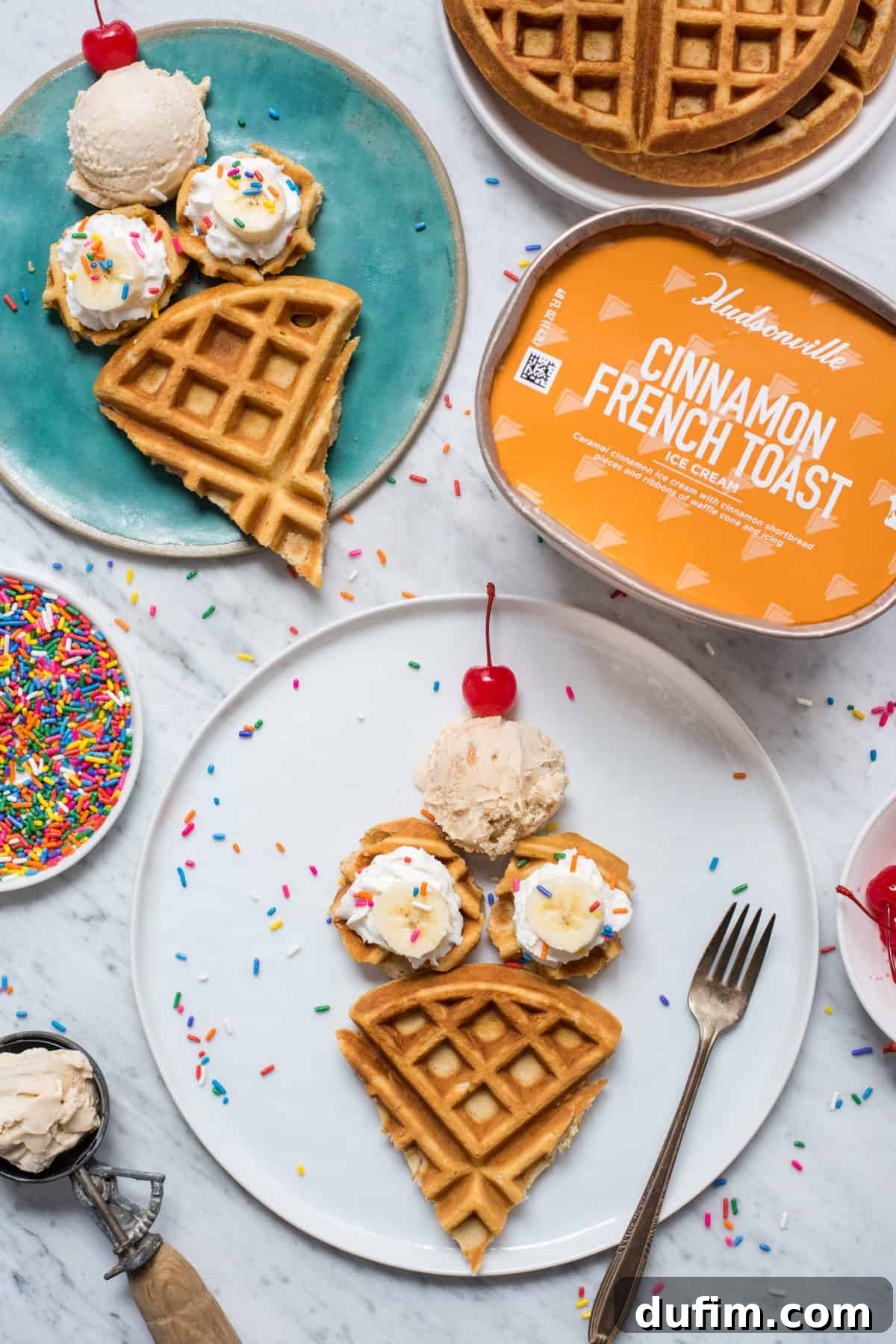 Two ice cream cone shaped waffles, each topped with whipped cream, banana slices, sprinkles, a scoop of ice cream, and a maraschino cherry, arranged on a white plate against a white background.