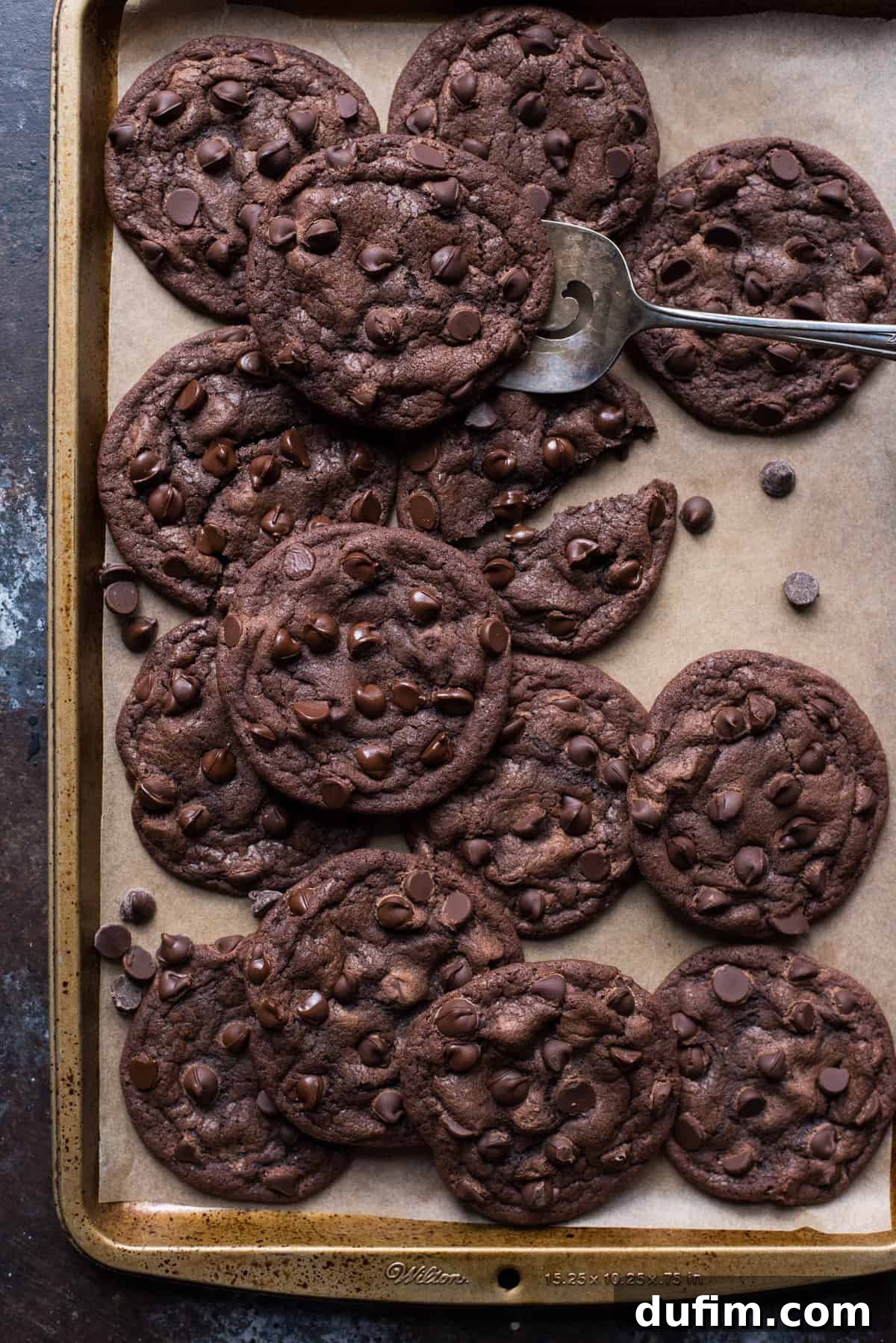 Double chocolate chip cookies neatly arranged on brown parchment paper, with a metal cookie spatula visible underneath one cookie.