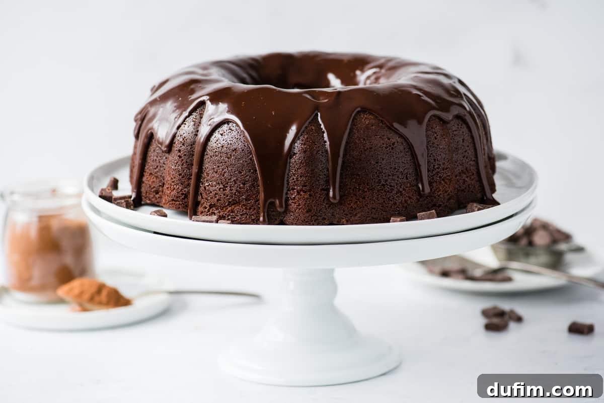 Decadent Chocolate Bundt with a Glossy Glaze 2 Whole chocolate bundt cake with glossy chocolate glaze on an elegant white cake stand, presented against a clean white background. Perfect for any celebration.