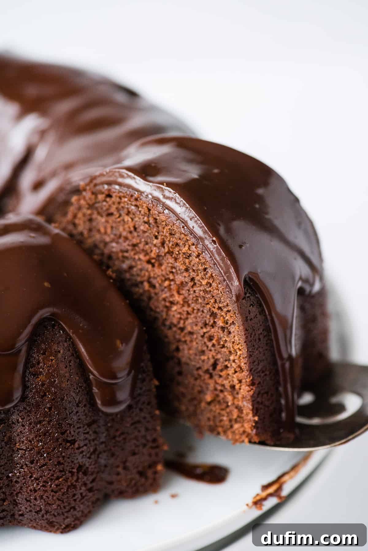 Decadent Chocolate Bundt with a Glossy Glaze 6 A second view of a slice of the rich chocolate bundt cake with glossy chocolate glaze being lifted by a metal spatula, ready to be served, highlighting its moist texture.