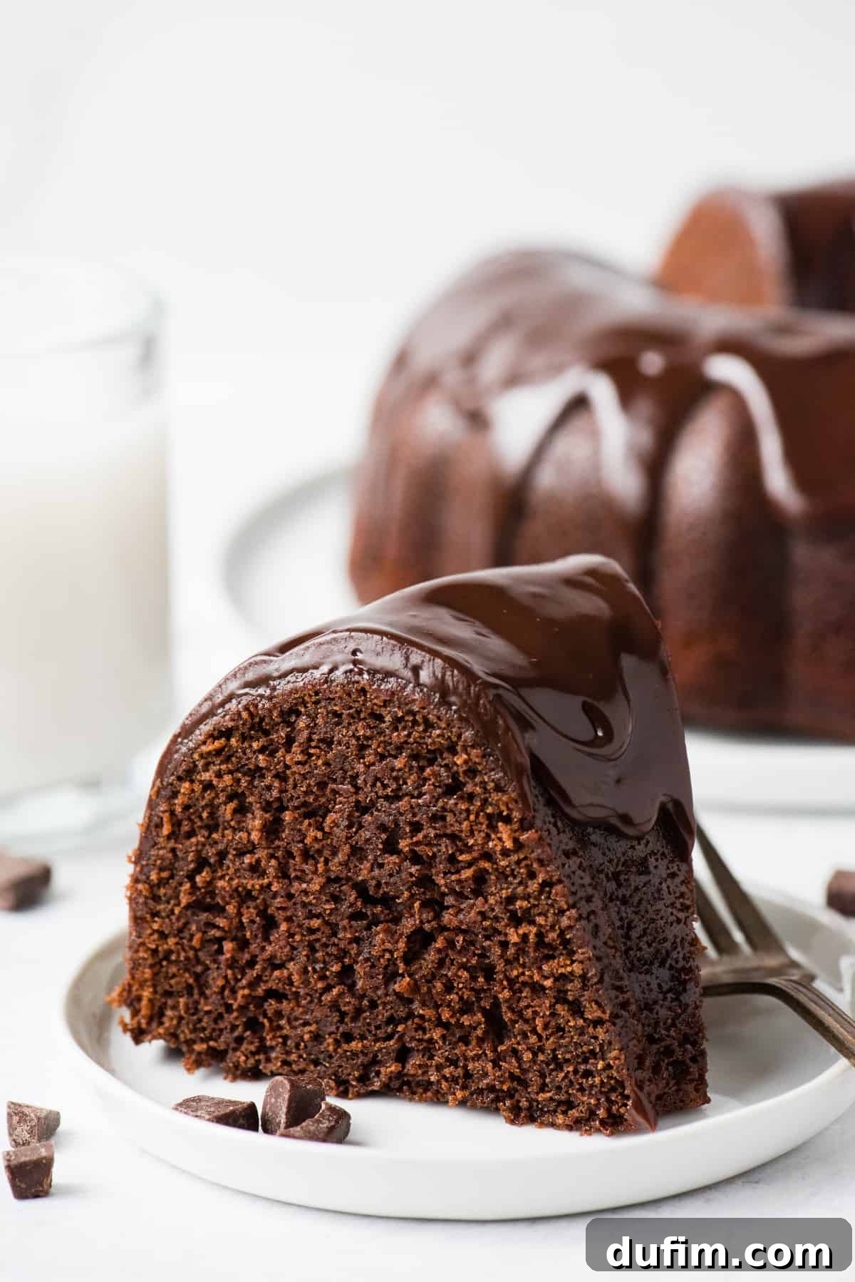 Decadent Chocolate Bundt with a Glossy Glaze 7 A perfect, individual slice of chocolate bundt cake, drenched in a generous amount of chocolate glaze, elegantly presented on a white plate against a minimalist white background.