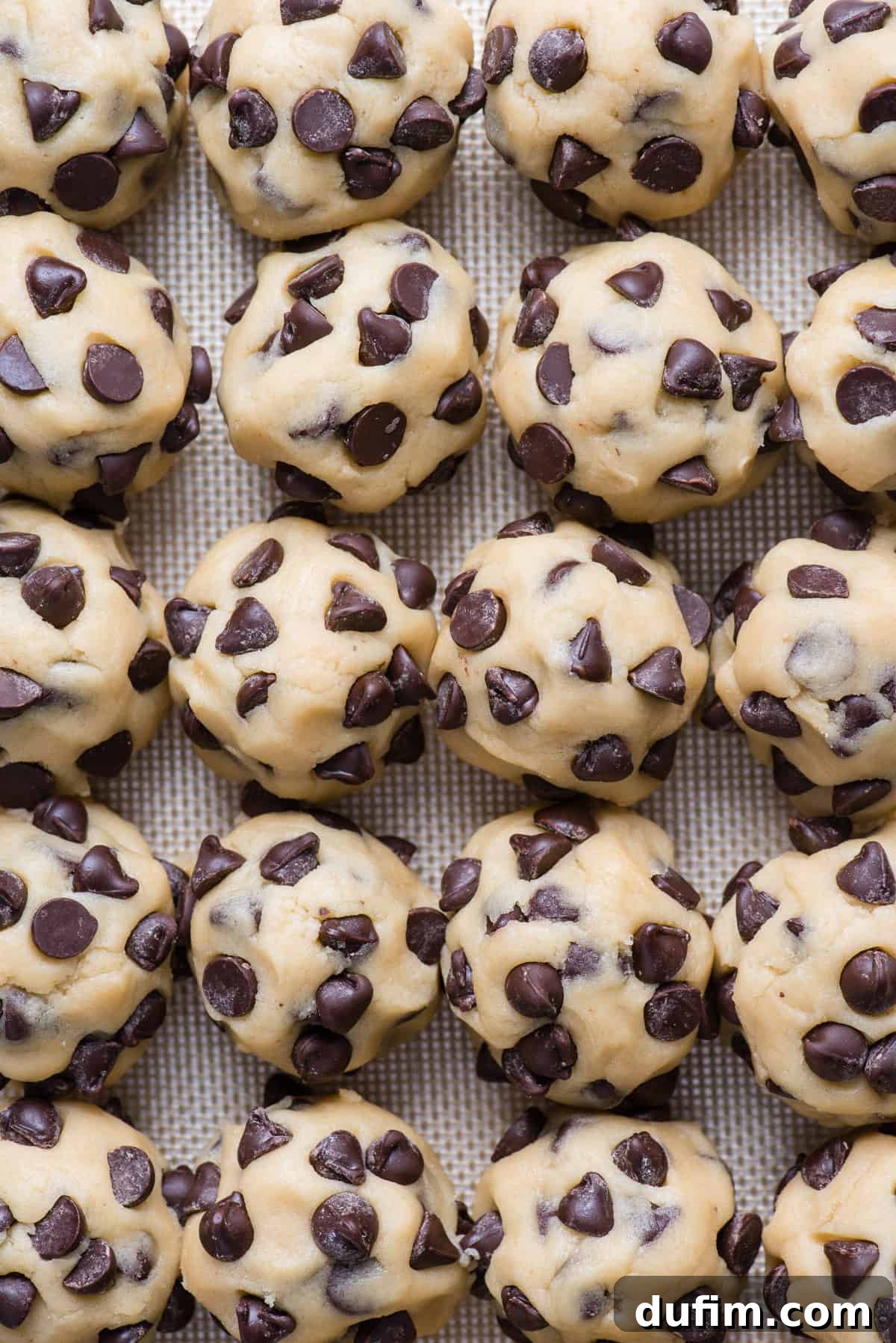 A grid pattern of perfectly formed chocolate chip cookie dough balls arranged neatly on a baking sheet, ready for freezing or baking.