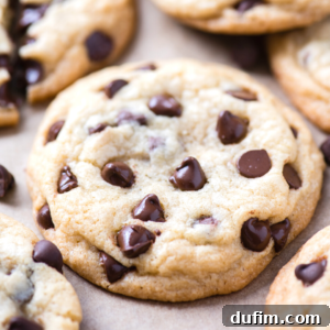 A close-up of several freshly baked chocolate chip cookies on a light brown surface, with melted chocolate chips peeking through the soft, golden-brown cookie dough—perfect for any chocolate chip cookies lover.