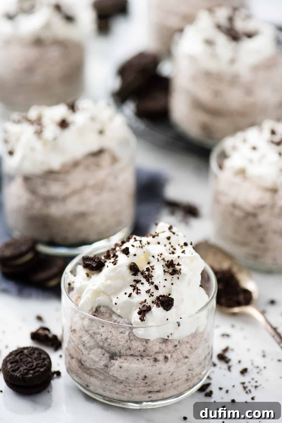 Single serving of creamy Oreo mousse in a clear glass dessert bowl, adorned with an elegant dollop of whipped cream and a sprinkle of crushed Oreo cookies, all set against a clean white background. This image showcases the simple elegance and irresistible appeal of the mousse, ready to be enjoyed.