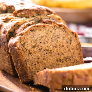 A close-up of easy banana bread, sliced on a wooden cutting board, highlights its moist and dense texture with a golden-brown crust.