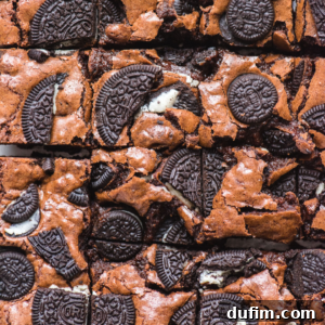 Decadent Oreo Fudge Brownies 9 Close-up of Oreo brownies topped with pieces of chocolate sandwich cookies, some whole and some broken, creating a rich, textured surface. The brownies are cut into squares.