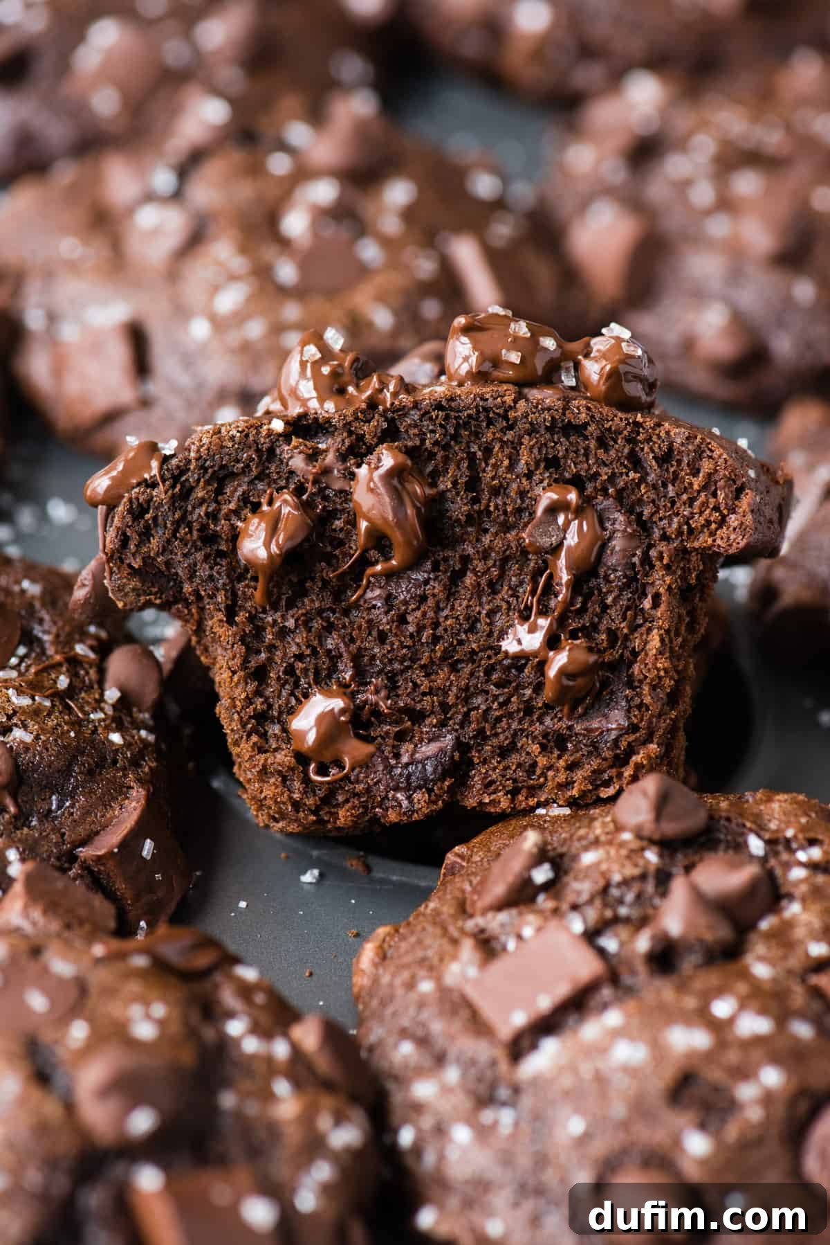 Decadent Chocolate Muffins 3 A chocolate muffin, freshly baked and cut in half, reveals a wonderfully moist interior filled with pockets of melted chocolate chips, resting in a metal muffin pan.
