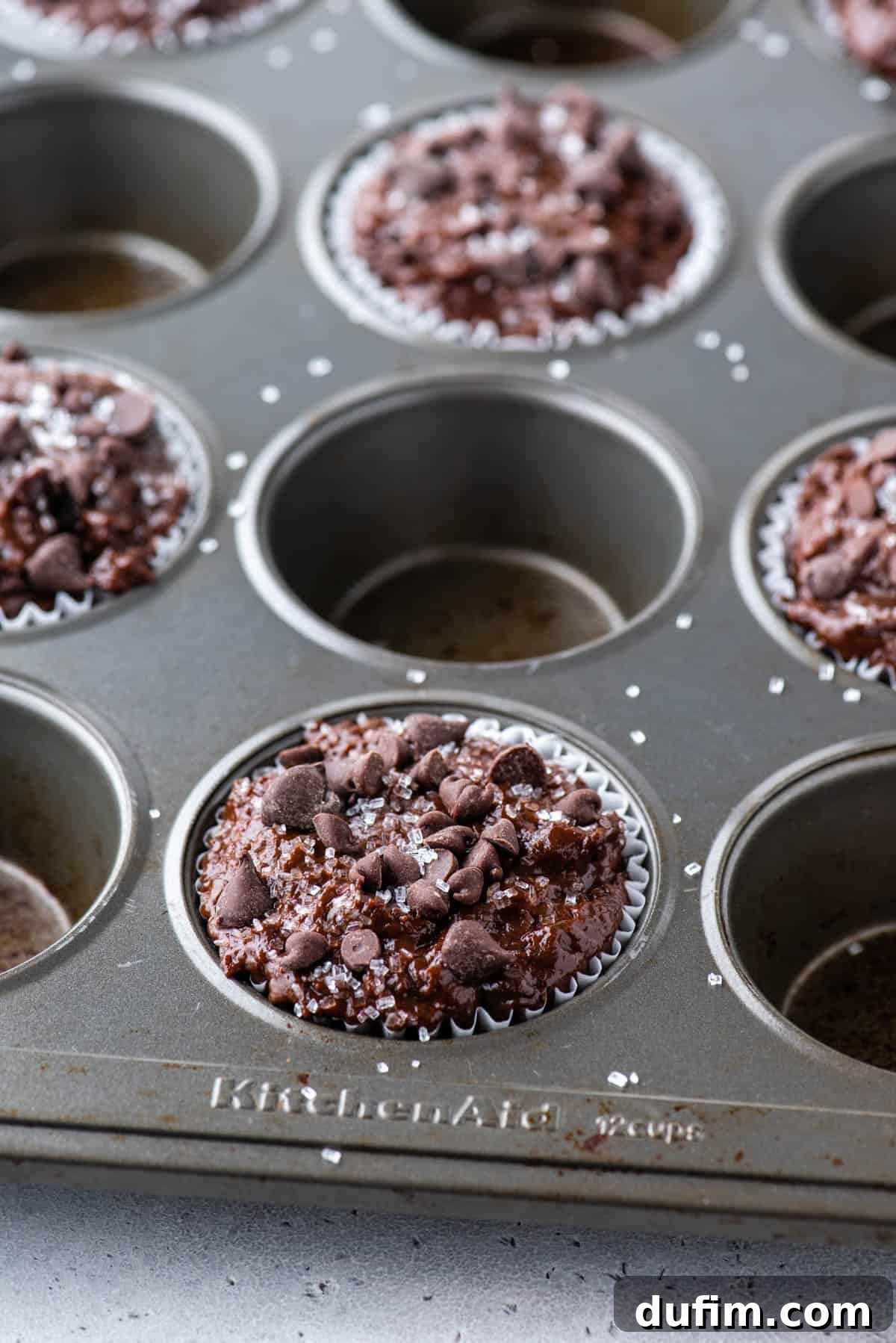 Decadent Chocolate Muffins 5 A muffin pan with every other cup filled generously with thick, rich chocolate muffin batter, ready for baking.