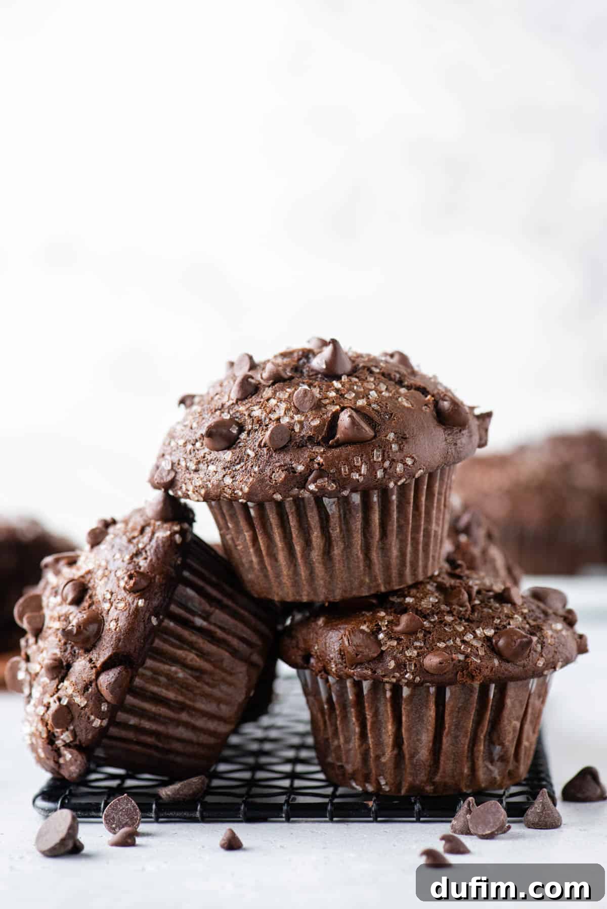 Decadent Chocolate Muffins 9 A stack of delicious chocolate muffins cooling on a black wire rack, showcasing their fluffy texture and enticing chocolate chips.