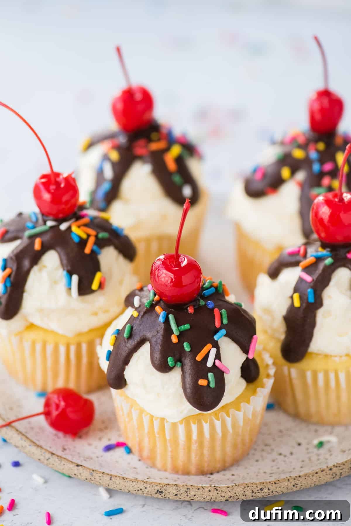 A collection of ice cream cupcakes artfully arranged on a white speckled plate against a clean white background, showcasing their festive and appealing presentation.