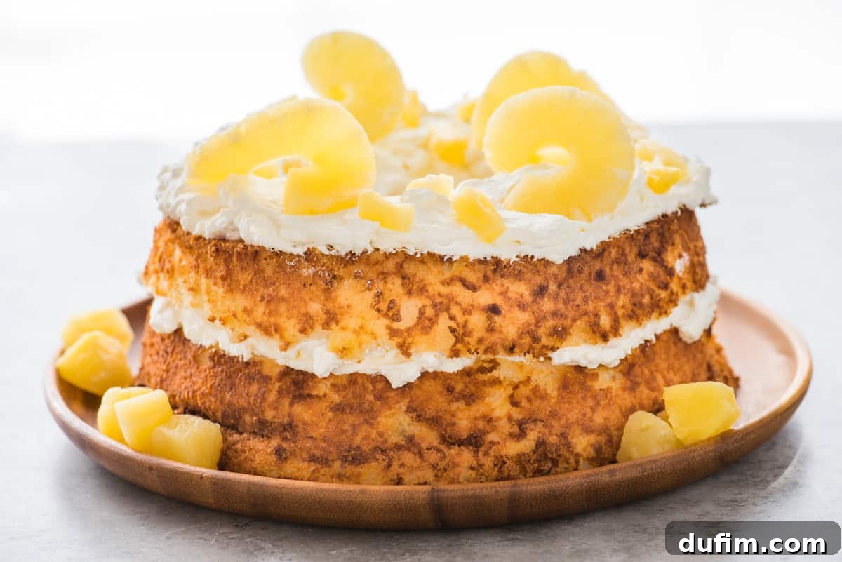 A beautifully decorated whole angel food cake topped with swirls of whipped cream and fresh pineapple slices, served on a rustic wooden tray.