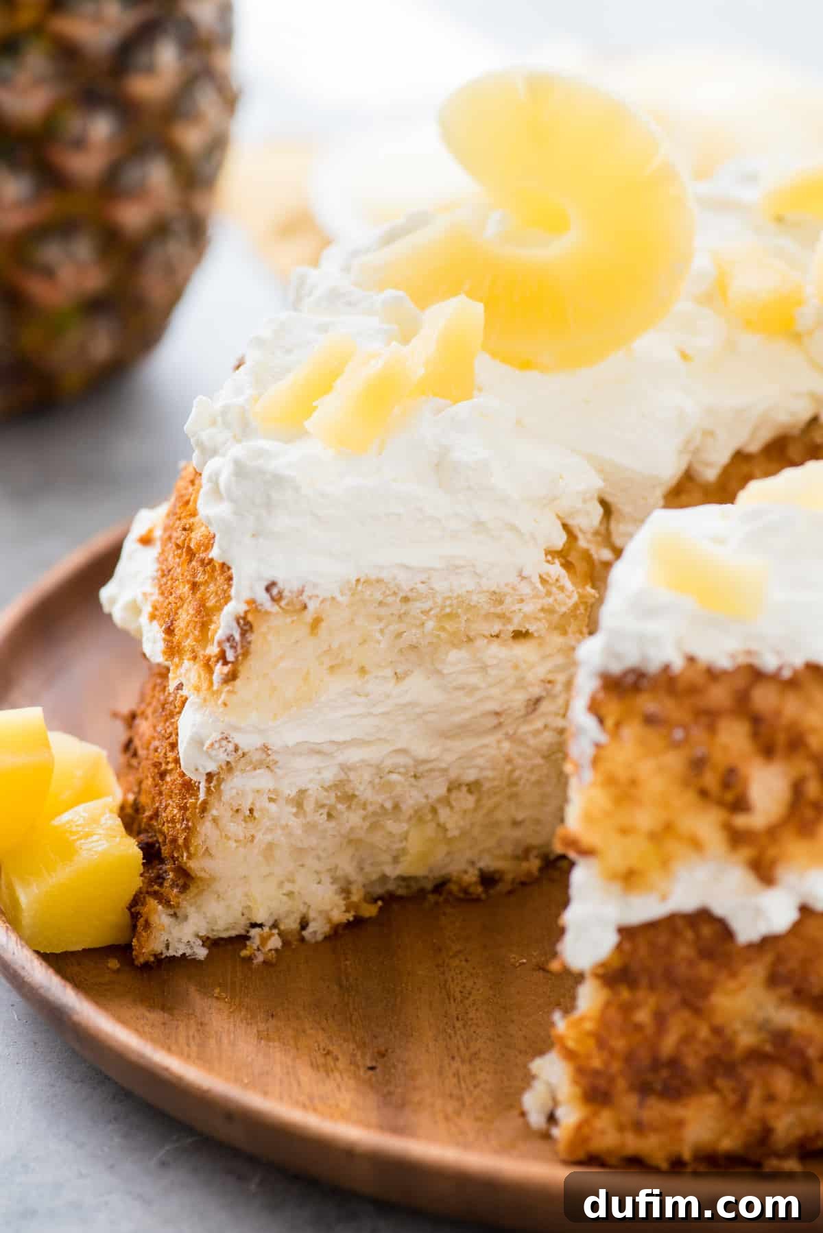 A slice of Pineapple Angel Food Cake removed from a larger cake, showing the layers of fluffy cake, whipped cream, and pineapple pieces.