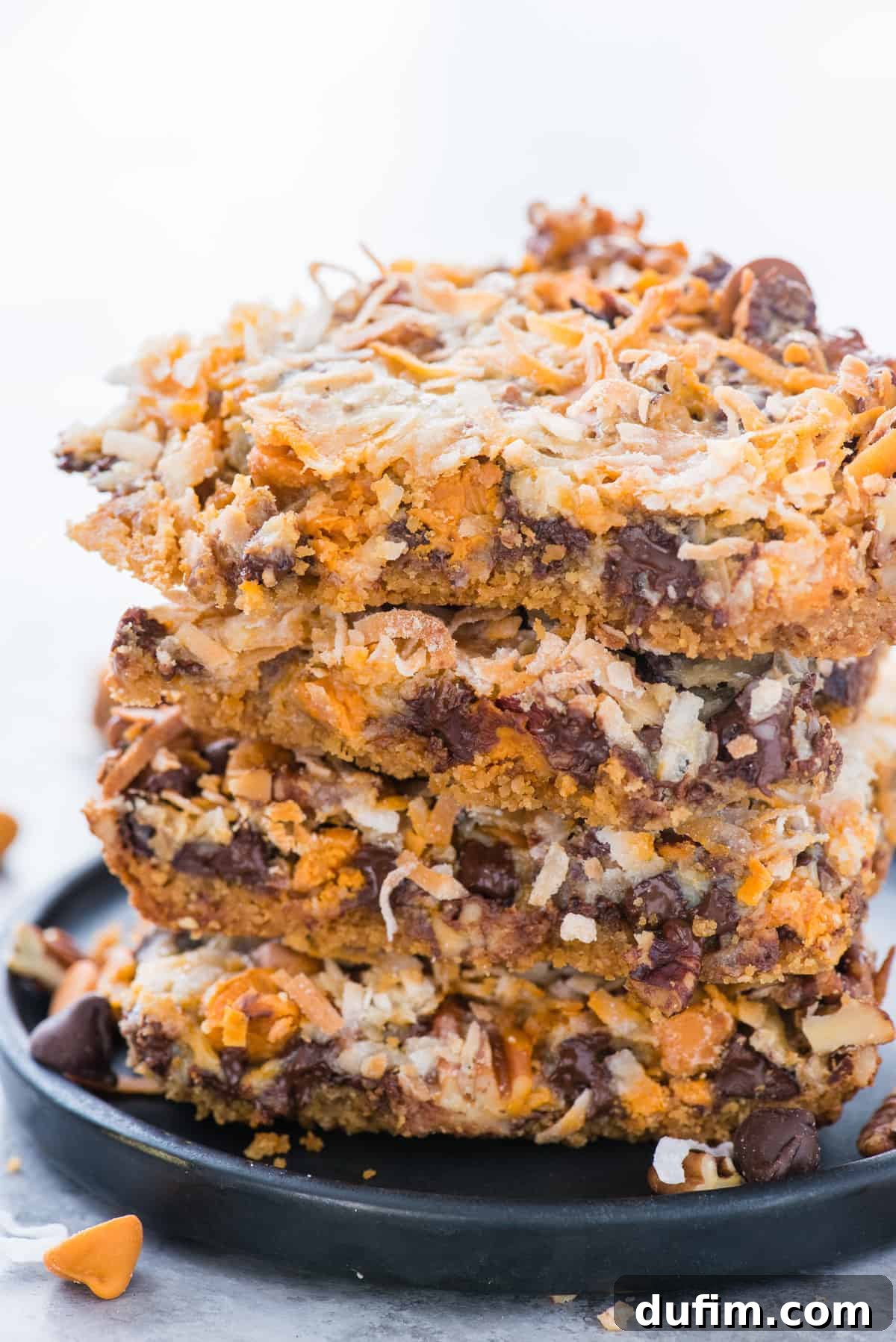 7 layer bars cut into squares stacked on top of each other on dark blue plate with white background