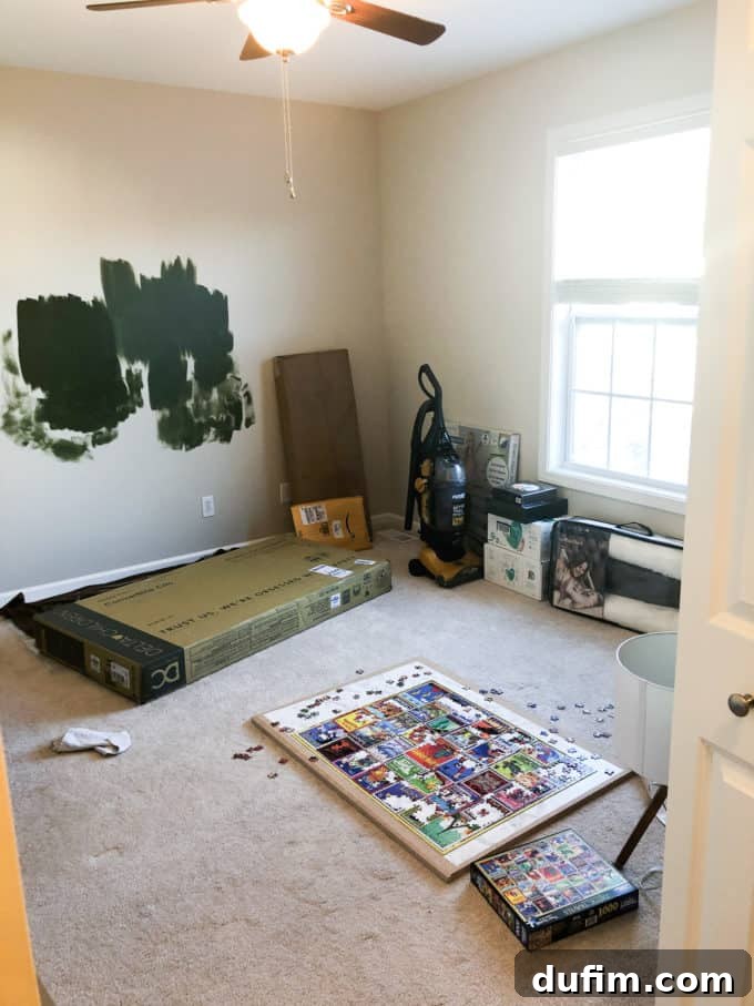 A room transitioning into a baby nursery, with paint samples on the wall and baby supplies beginning to accumulate.
