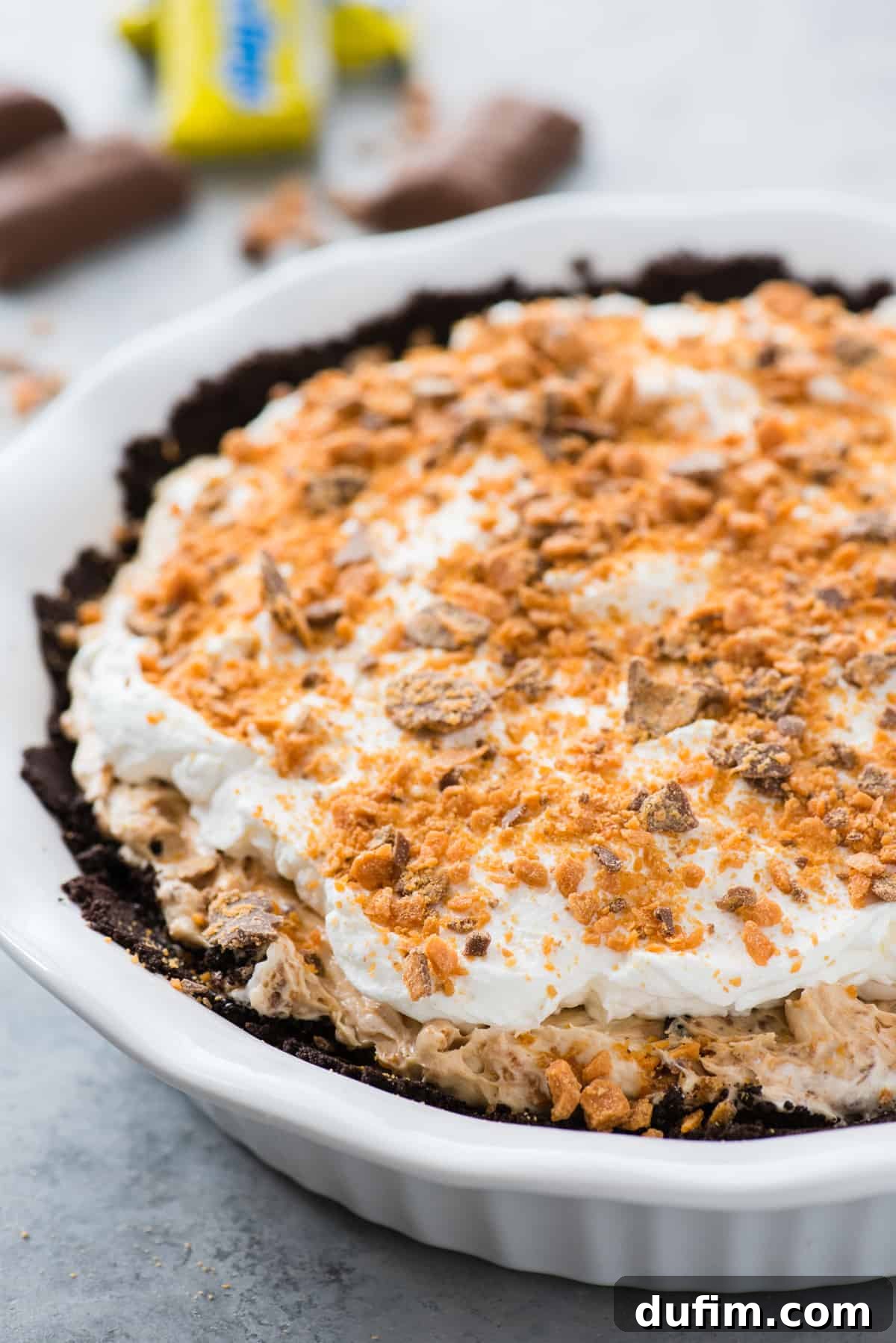 Butterfinger Crunch Pie 3 A whole Butterfinger pie in a white pie pan, perfectly set and ready to be served, against a soft gray background.