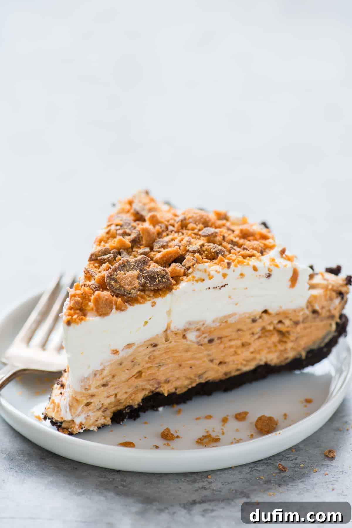 Butterfinger Crunch Pie 6 A beautiful slice of Butterfinger pie served on a pristine white plate, set against a stylish gray background, highlighting its rich layers and inviting appeal.