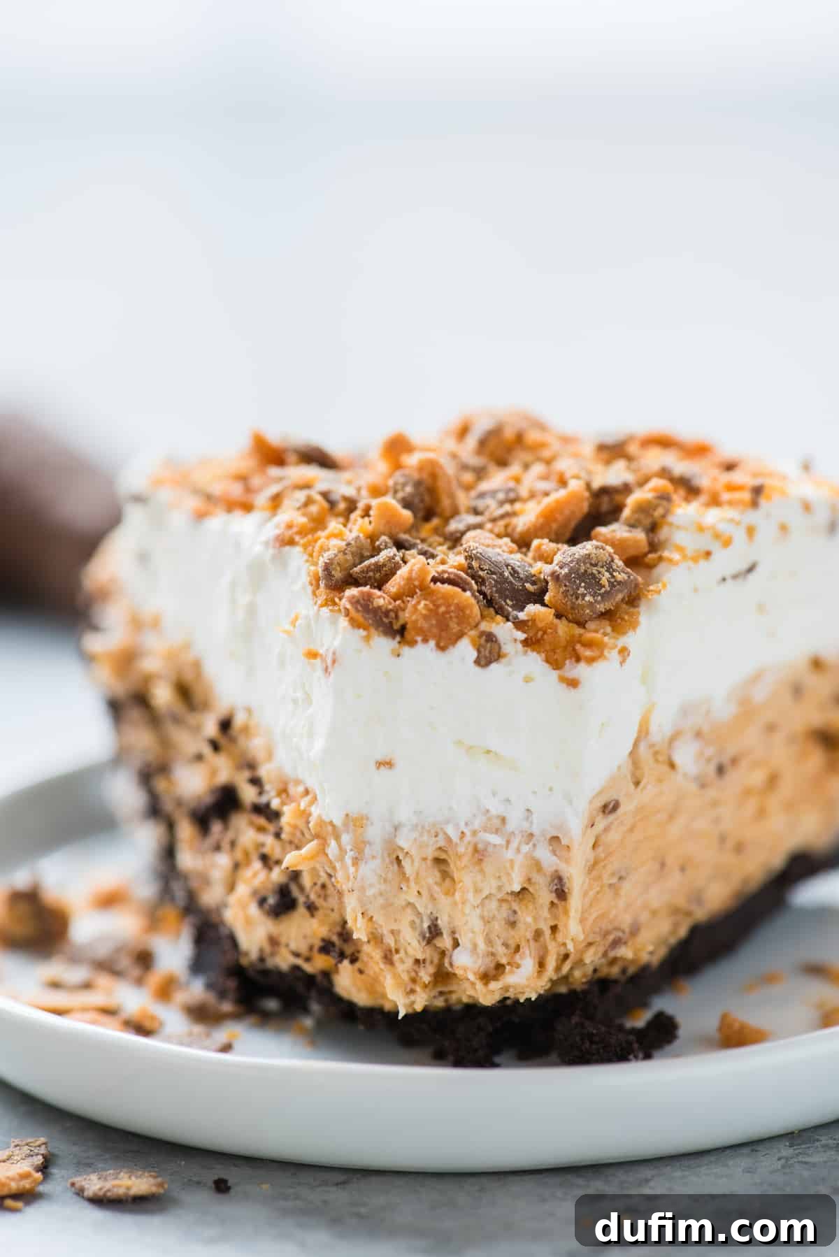 Butterfinger Crunch Pie 8 A close-up of a slice of Butterfinger pie on a white plate with a bite removed, showing the creamy filling and crunchy crust.