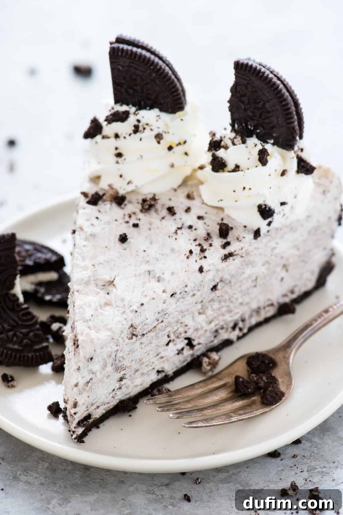 A pristine slice of no-bake Oreo cheesecake presented on a simple white plate, perfectly showcasing its distinct layers of creamy filling and rich, dark Oreo crust. A fork rests beside it, ready for indulgence.