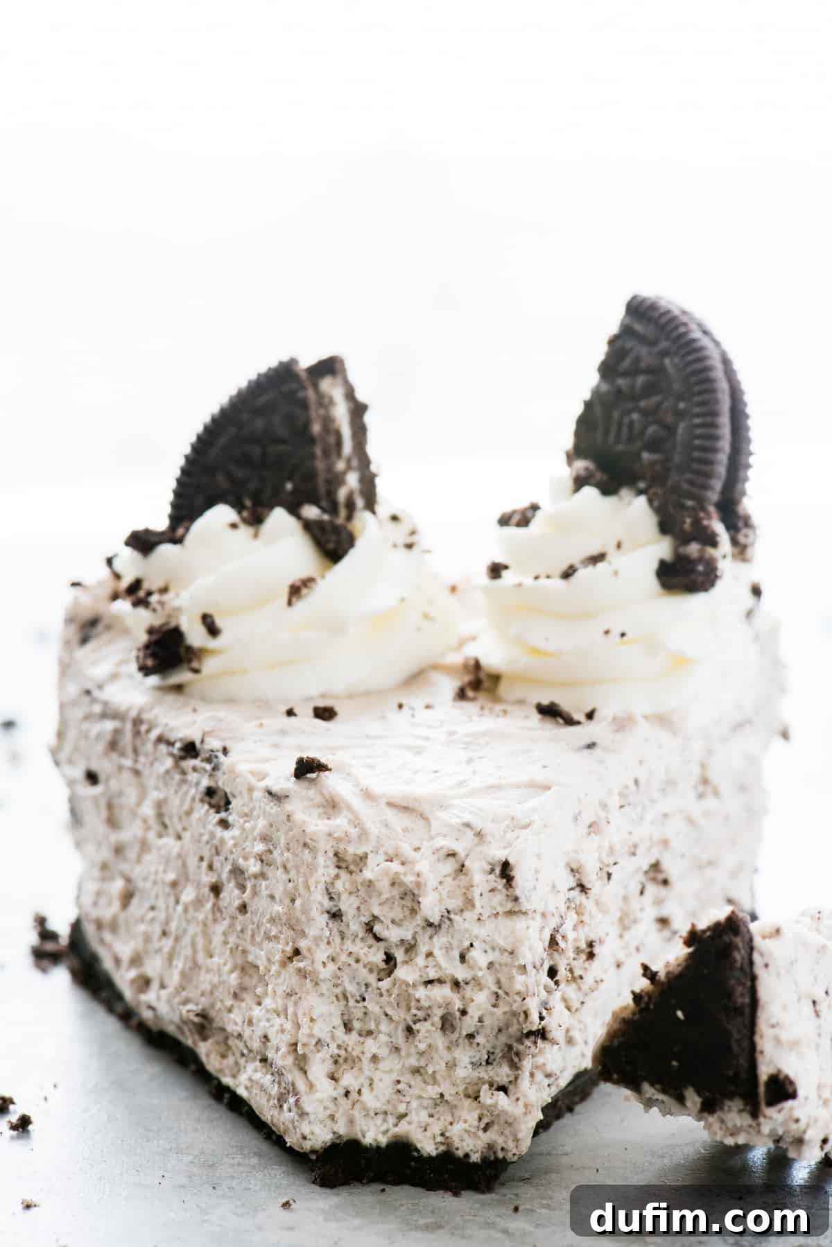 A delicious slice of no-bake Oreo cheesecake with a bite taken out, resting on a white background, highlighting its fluffy texture and the generous Oreo crumbles.