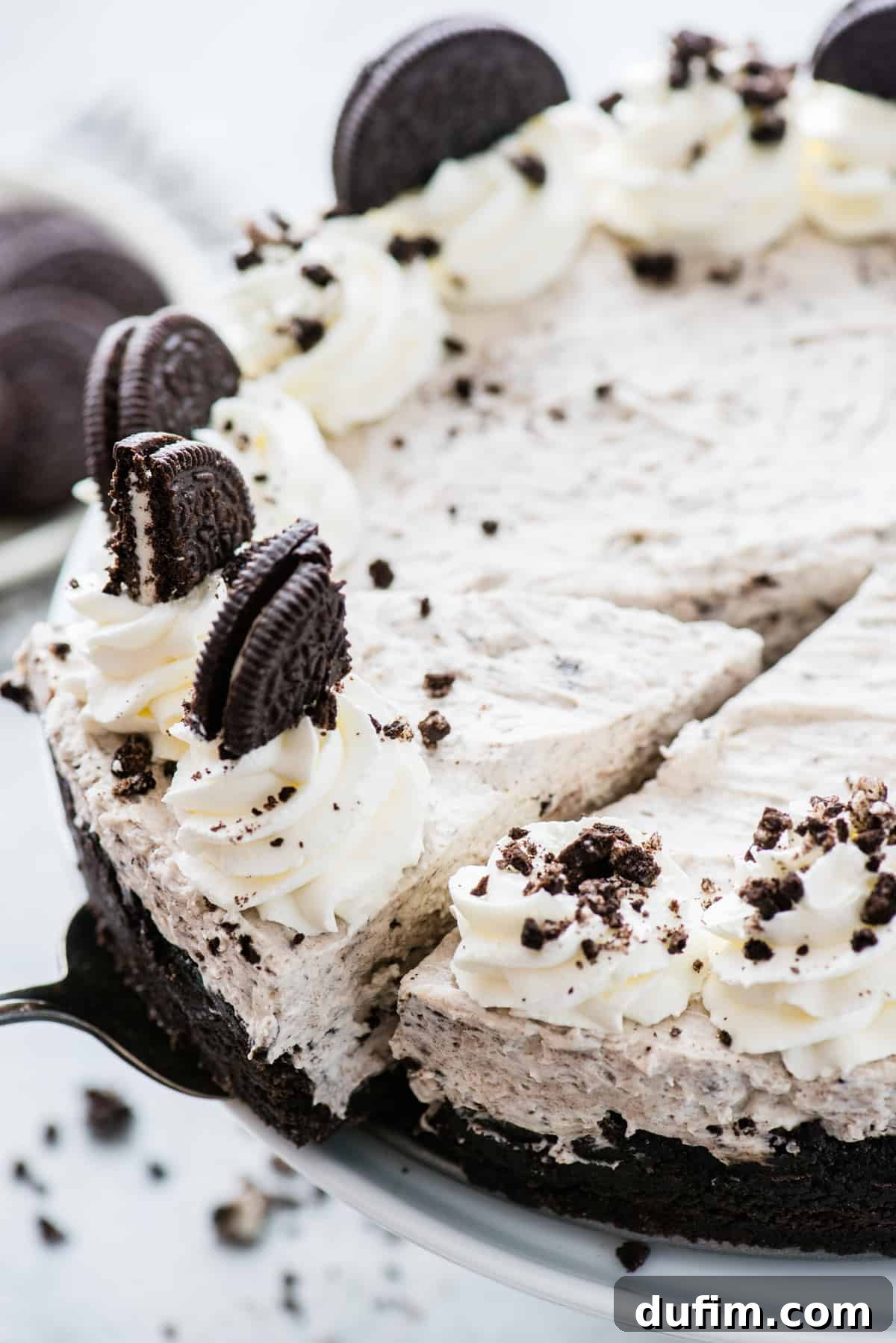 Another view of the complete no-bake Oreo cheesecake, featuring its decadent whipped cream topping and scattered Oreo pieces, set against a clean white background, ready to be served.