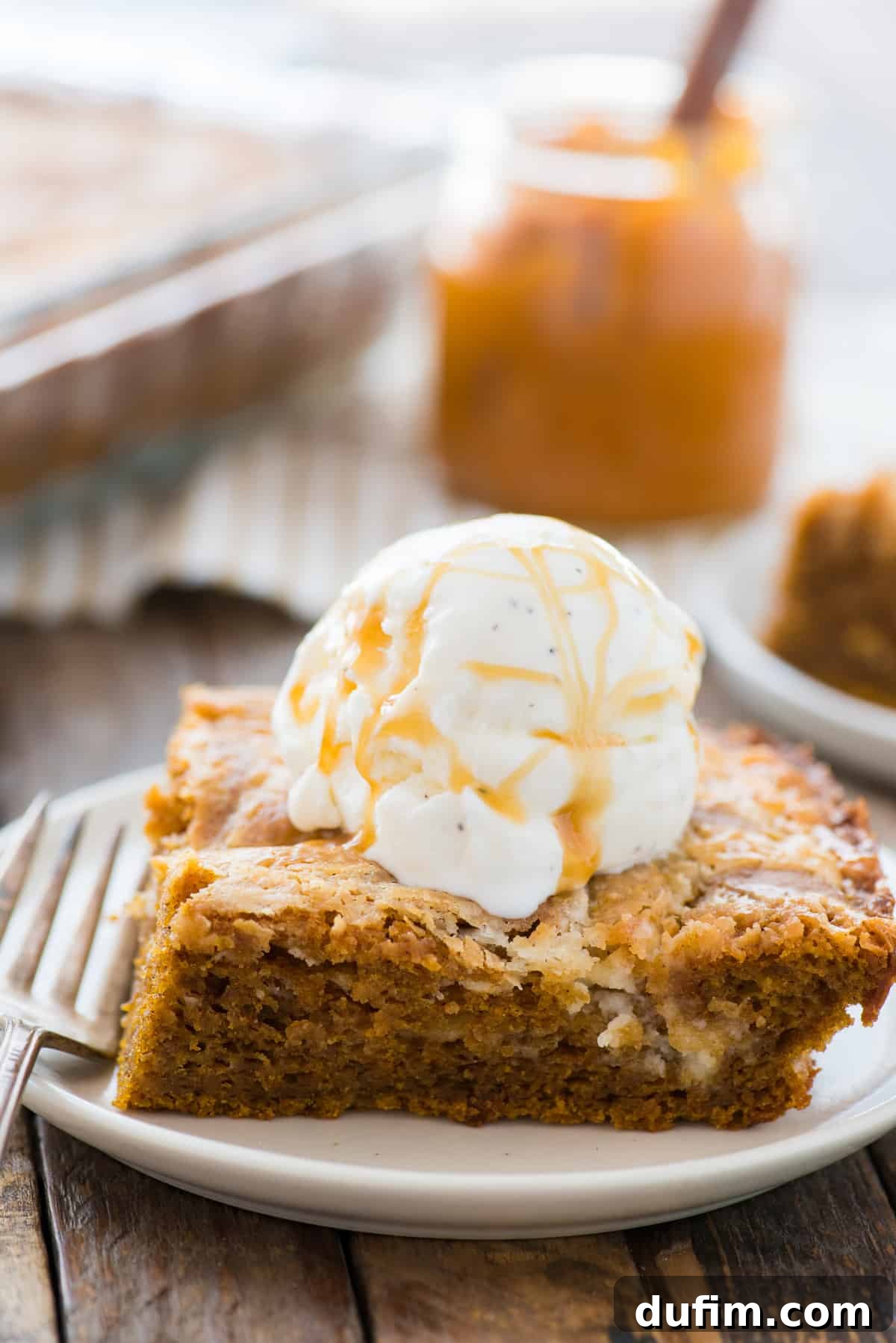 Spiced Pumpkin Earthquake Cake 2 A perfectly sliced piece of pumpkin earthquake cake rests on a white plate, adorned with a generous scoop of creamy vanilla ice cream. The cake's rich, moist interior and the tantalizing cream cheese swirl are clearly visible, inviting a taste of fall comfort.