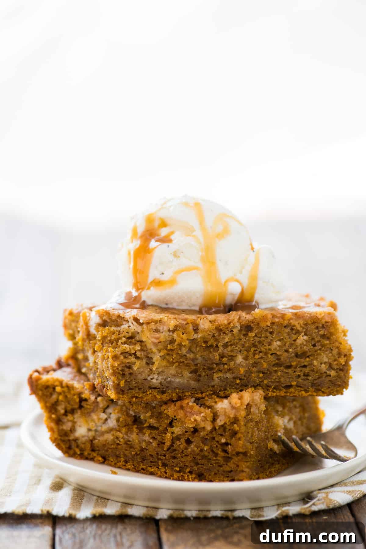 Spiced Pumpkin Earthquake Cake 6 Two generous slices of pumpkin earthquake cake are artfully stacked on a white plate, each topped with a dollop of vanilla ice cream. The visual emphasizes the cake's height, texture, and the irresistible combination of warm cake and cold ice cream.