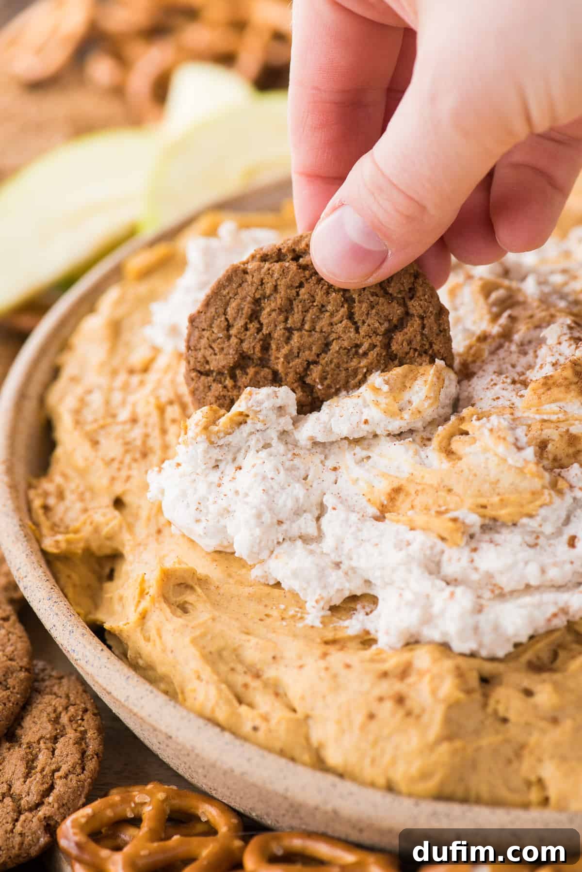 A close-up shot of the rich, creamy pumpkin dip in a bowl, with a hand elegantly dipping a spiced gingersnap cookie into the luscious topping, highlighting its inviting texture.