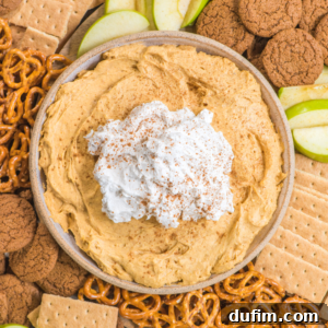 A bowl of creamy pumpkin pie dip topped with whipped cream and cinnamon, surrounded by green apple slices, pretzels, graham crackers, and gingersnap cookies.