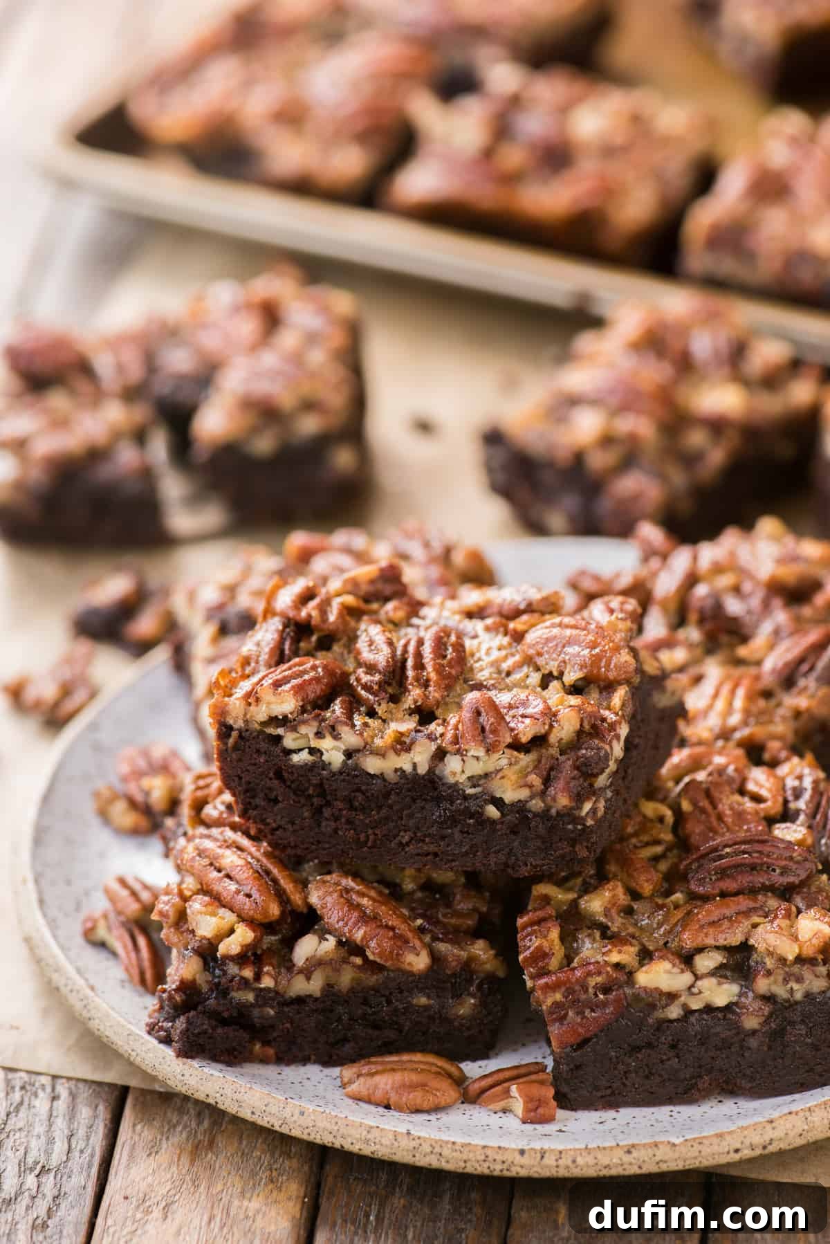 Caramel Pecan Brownie Bliss 2 Perfectly cut pecan pie brownies stacked on a white plate against a rustic wooden background, showcasing their fudgy chocolate base and glossy pecan topping.