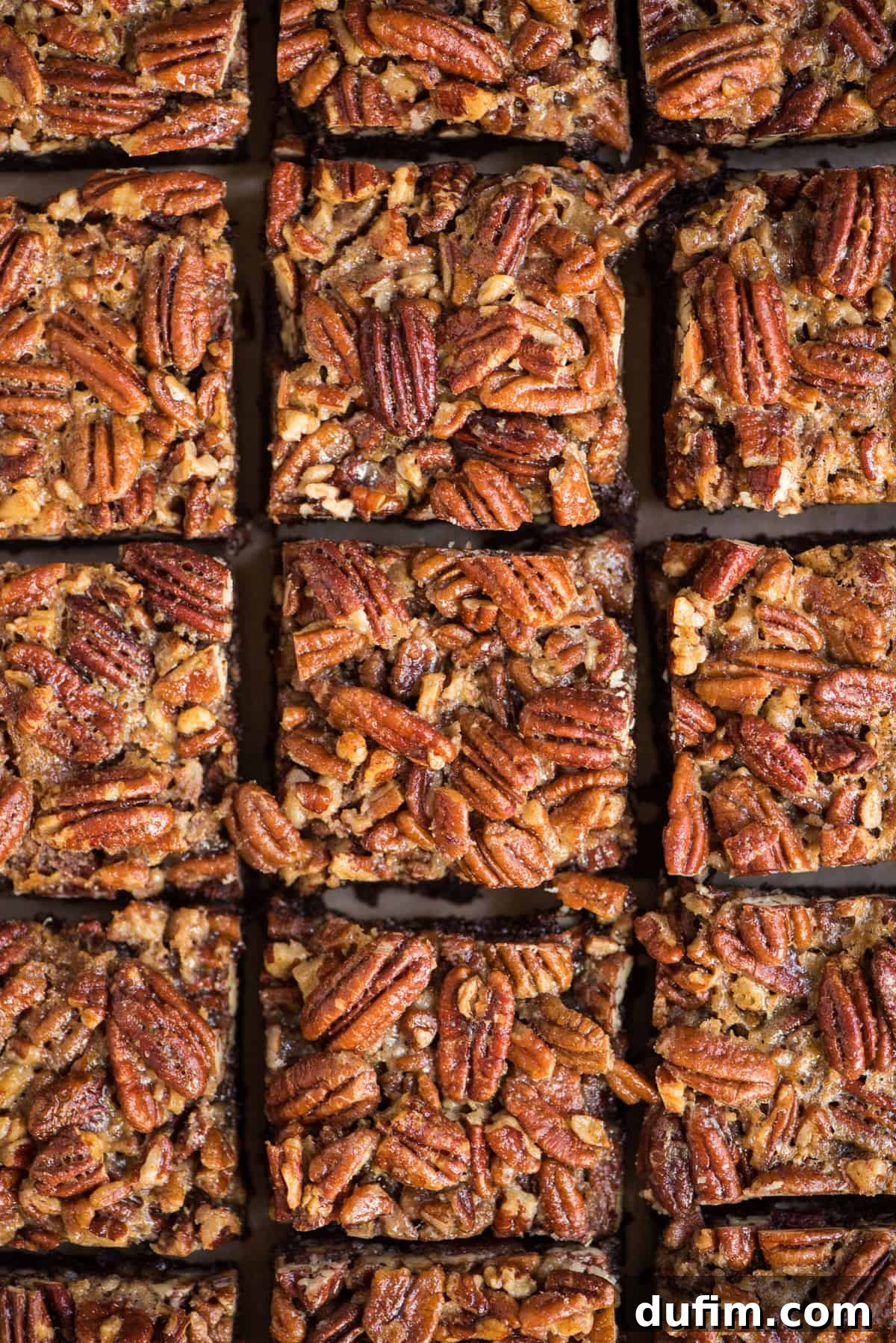 Pecan Pie Brownies neatly cut into squares and arranged in a grid pattern on a baking sheet, showcasing their even layers and golden pecan topping.