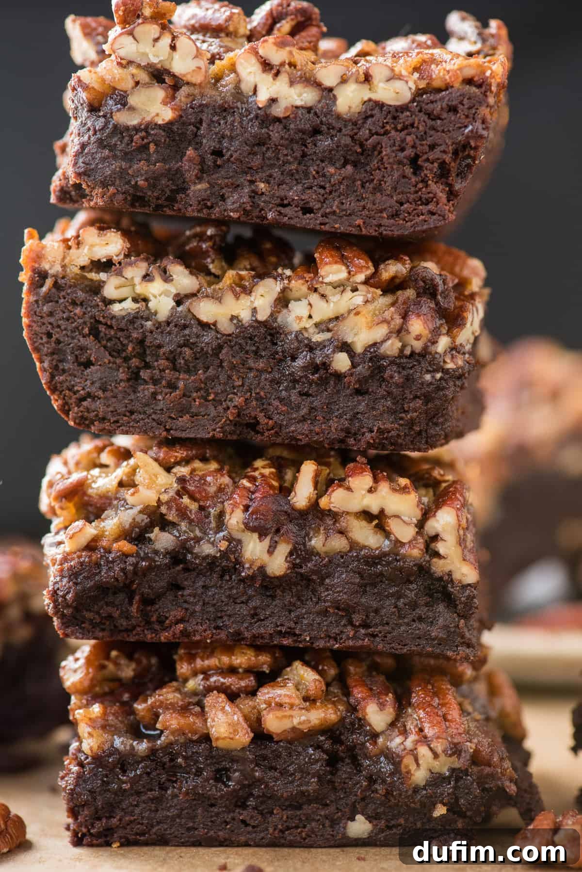 A close-up of several pecan pie brownies stacked atop each other, showcasing the glistening, rich pecan topping and the deep chocolate color of the brownie base.