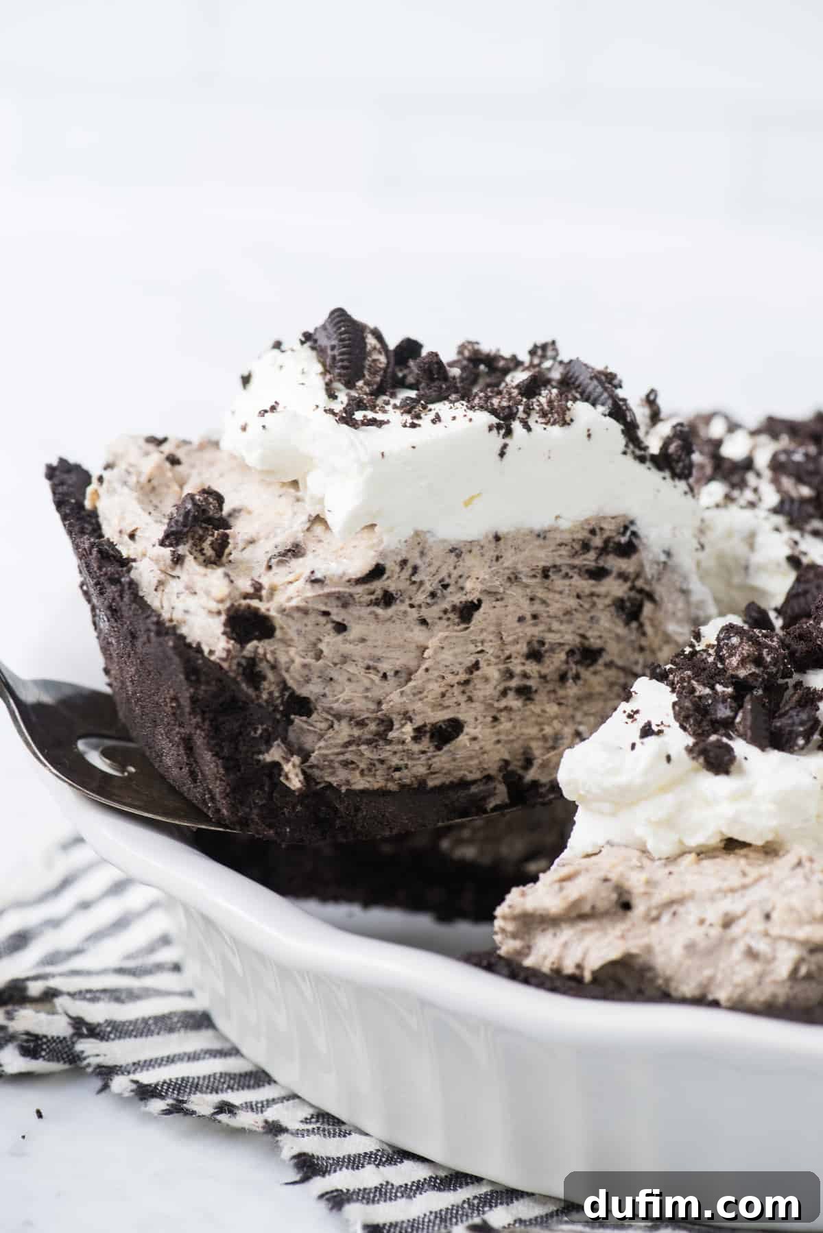 A slice of creamy Oreo pudding pie being carefully lifted from a pie dish, highlighting its generous filling and sturdy crust.