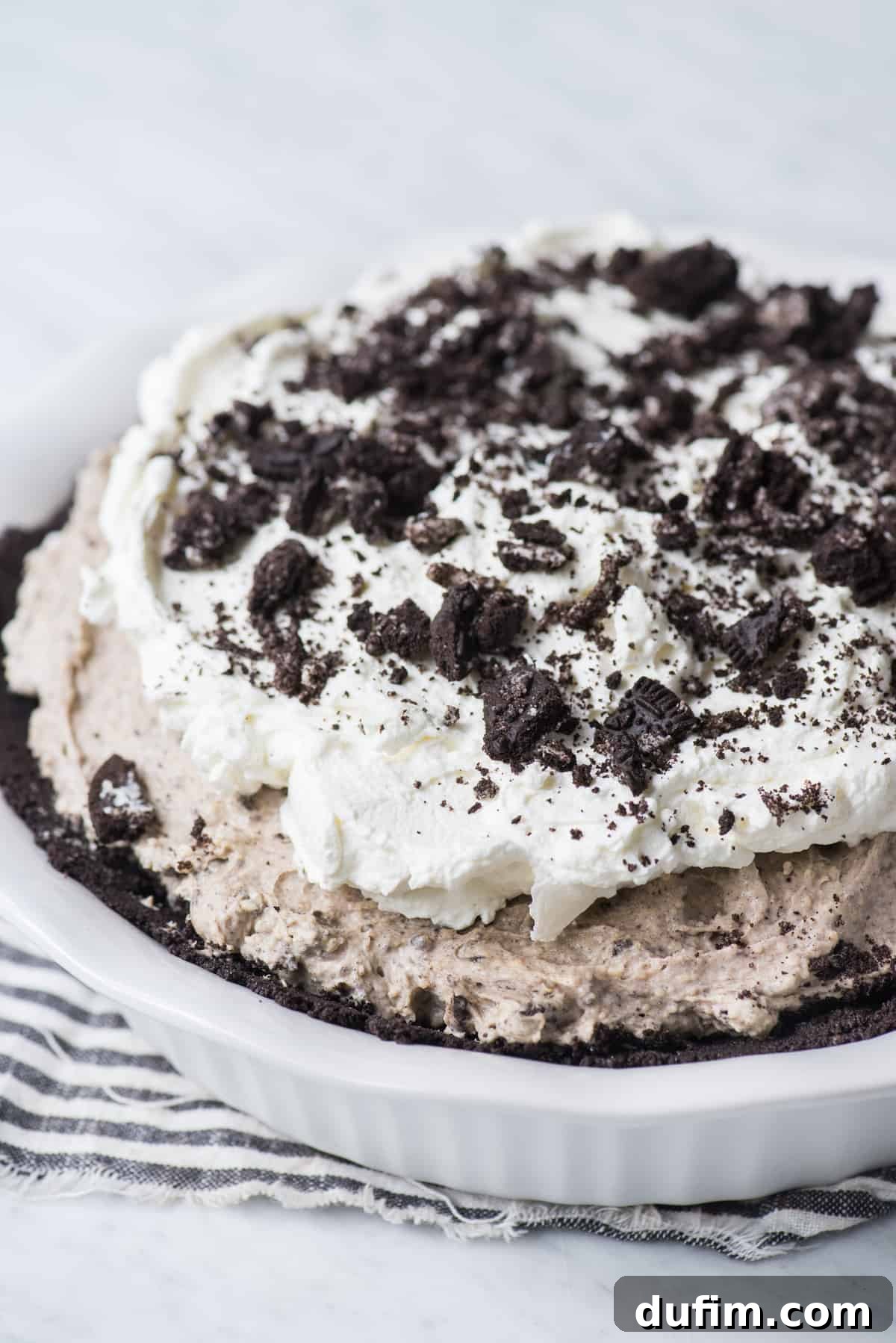 A whole no-bake Oreo pudding pie, elegantly topped with swirls of whipped cream and generously sprinkled with crushed Oreo pieces, ready to be served.