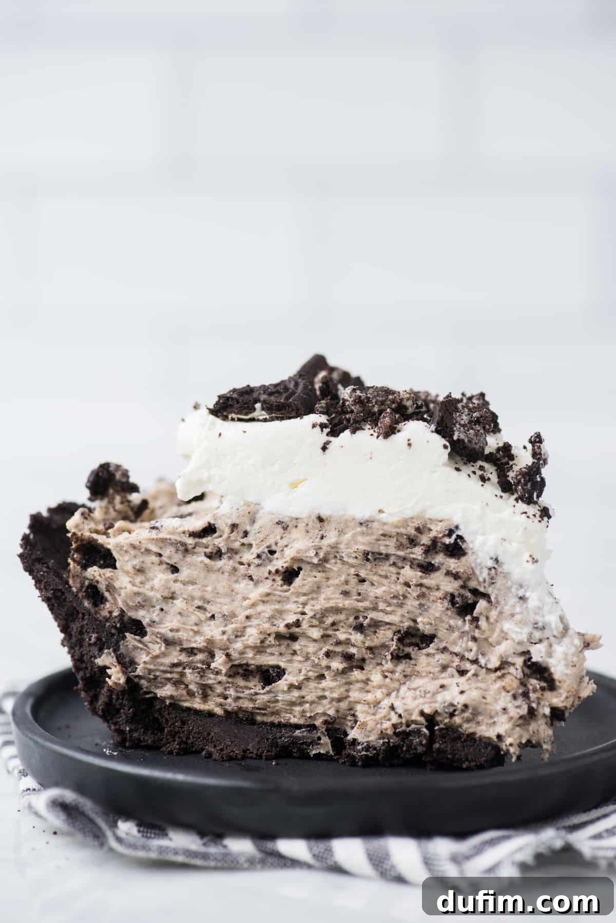 A single slice of Oreo pudding pie, presented on a sleek black plate against a soft white background, inviting a closer look at its delightful layers.