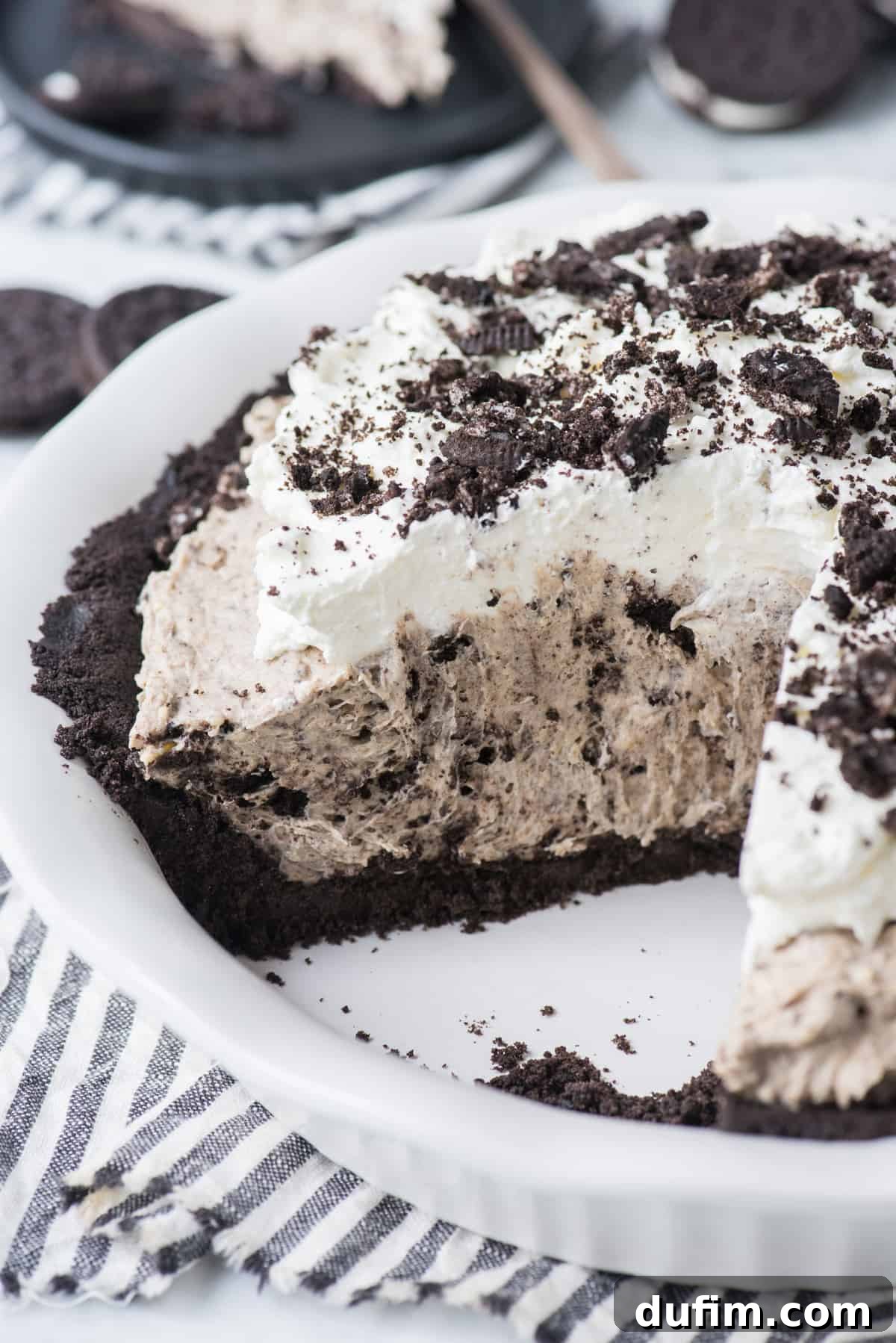 A stunning close-up of a slice of Oreo pudding pie on a black plate, with rich chocolate and creamy white layers, garnished with cookie crumbs.