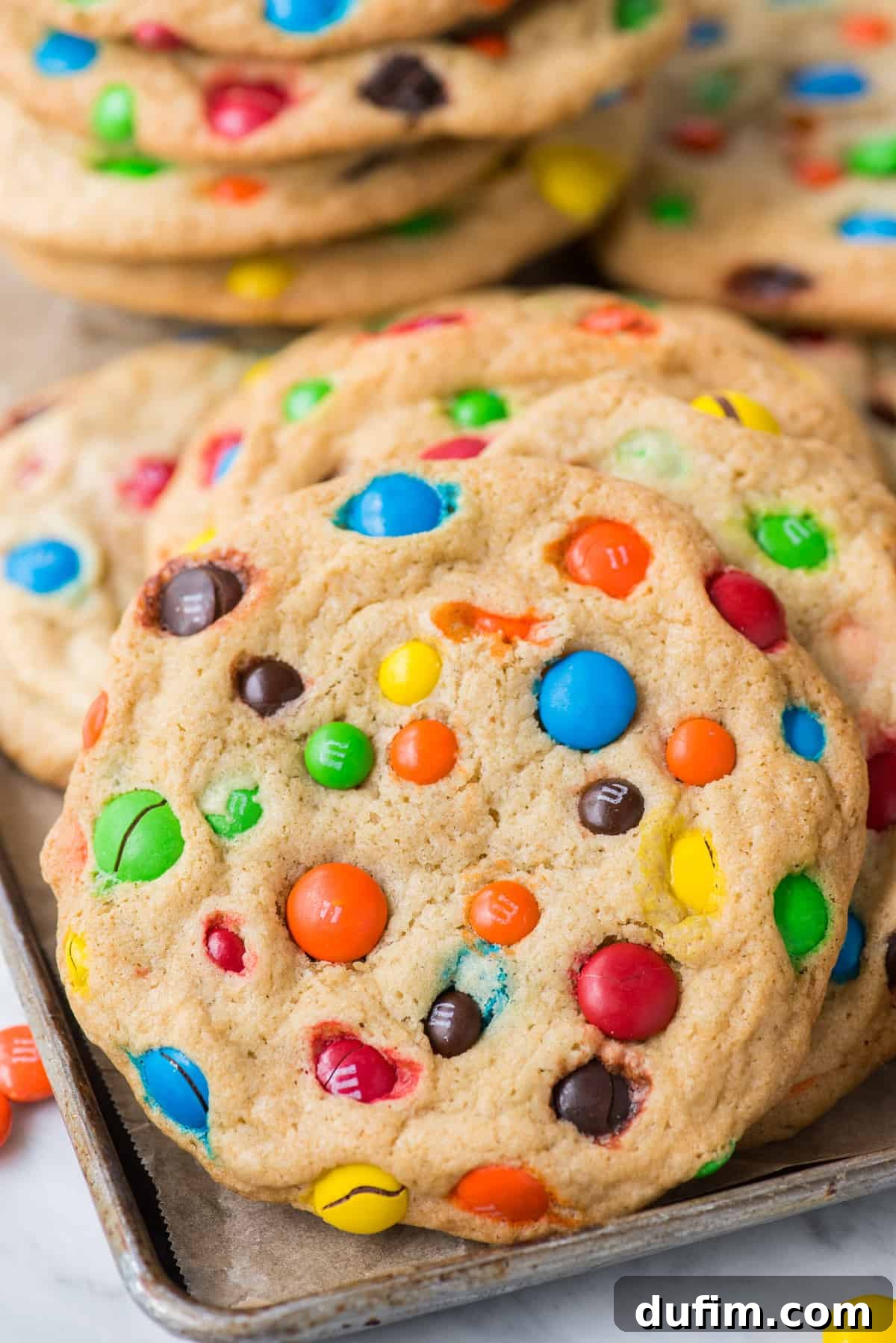 Chewy M&M Cookie Recipe 7 M&M cookies propped up on metal baking sheet, ready to be served