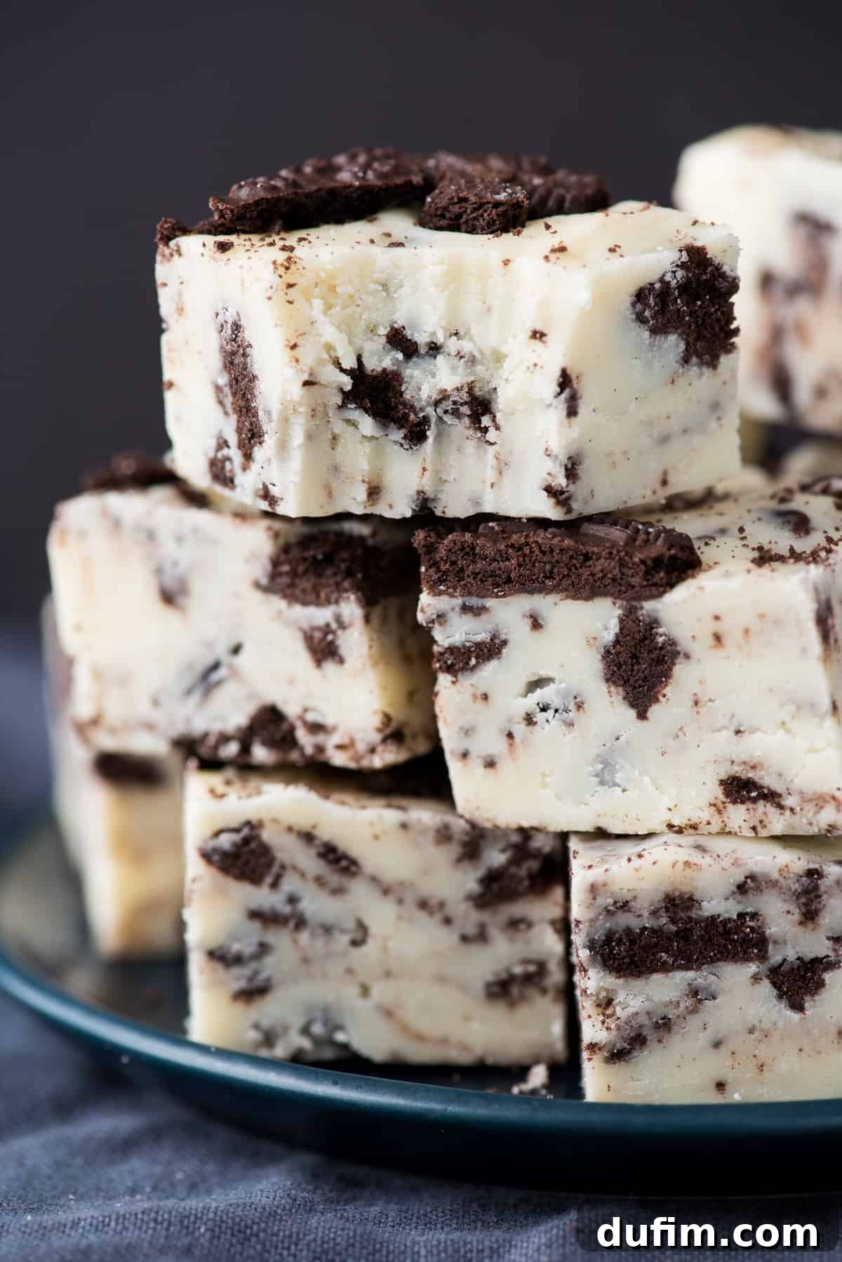 Decadent Oreo Fudge 6 Beautifully cut Oreo fudge squares stacked on top of each other against a dark background, highlighting the creamy texture and cookie pieces
