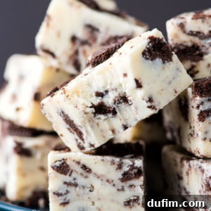 Close-up of stacked white chocolate oreo fudge cubes, with chocolate cookie pieces mixed throughout, creating a marbled appearance. The texture is creamy and smooth with visible cookie chunks.
