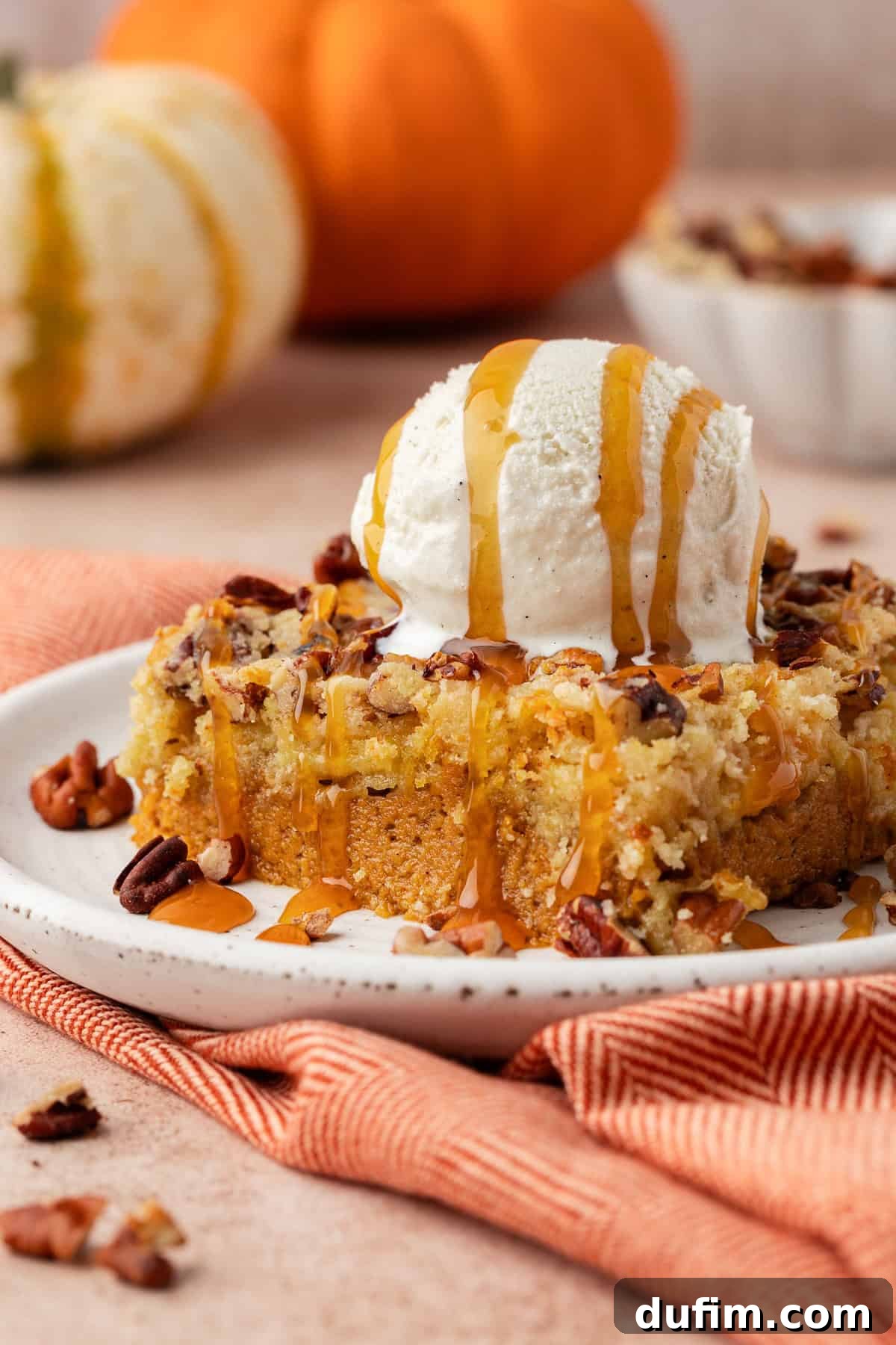 Effortless Autumn Pumpkin Dump Cake 12 A perfectly portioned slice of warm pumpkin dump cake on a white plate, elegantly topped with a generous dollop of fresh whipped cream and a delicate sprinkle of cinnamon.