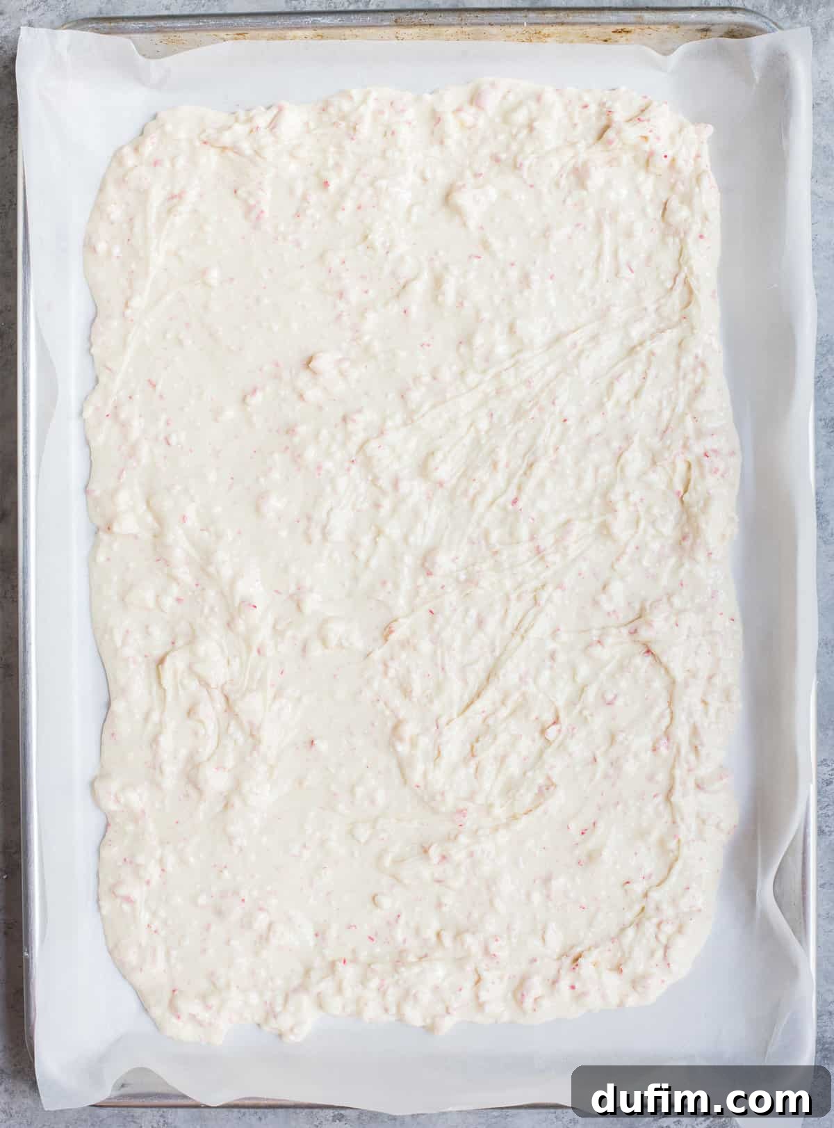 Frosted Peppermint Dream Bark 4 Smooth layer of melted white chocolate peppermint bark spread evenly on parchment paper on a baking sheet.