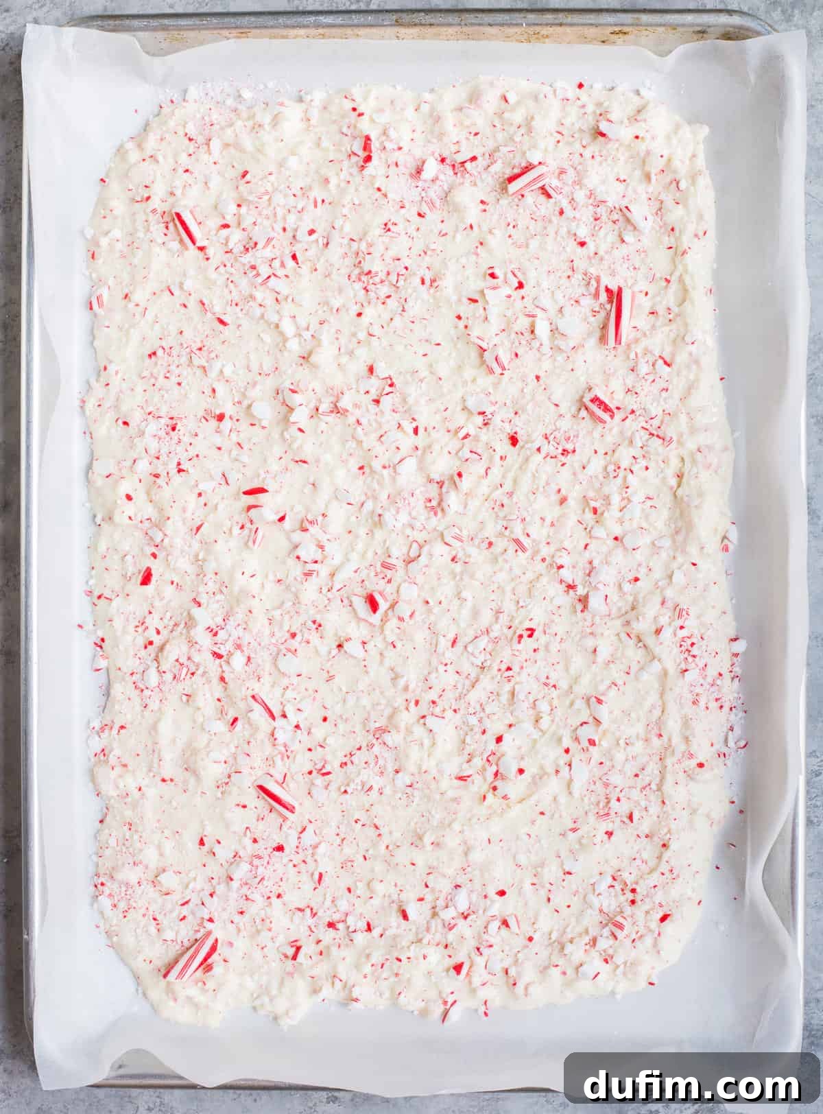 Frosted Peppermint Dream Bark 5 Melted white chocolate peppermint bark evenly spread on parchment paper, sprinkled with crushed candy canes.