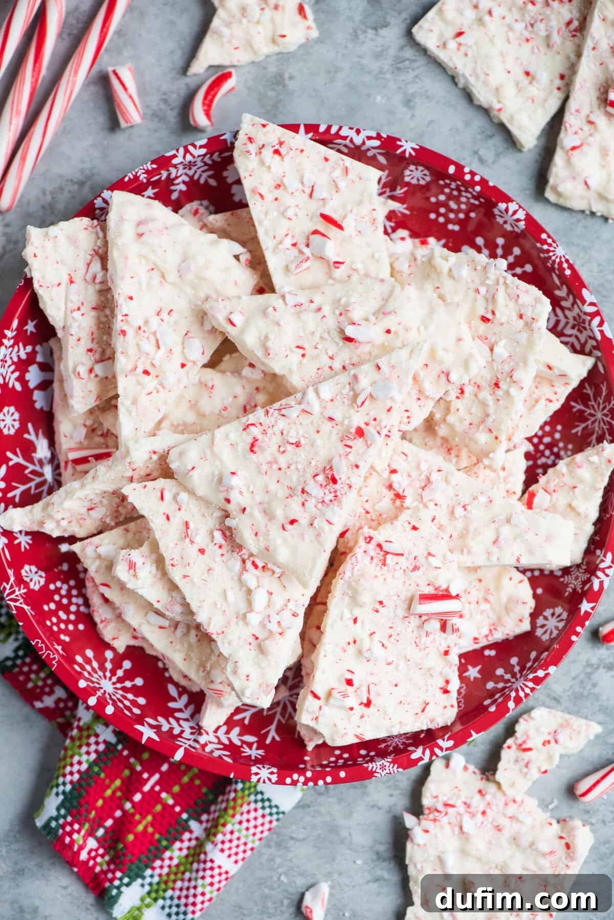 Frosted Peppermint Dream Bark 6 Pieces of white chocolate peppermint bark, broken into irregular shapes, artfully arranged on a festive red Christmas plate.