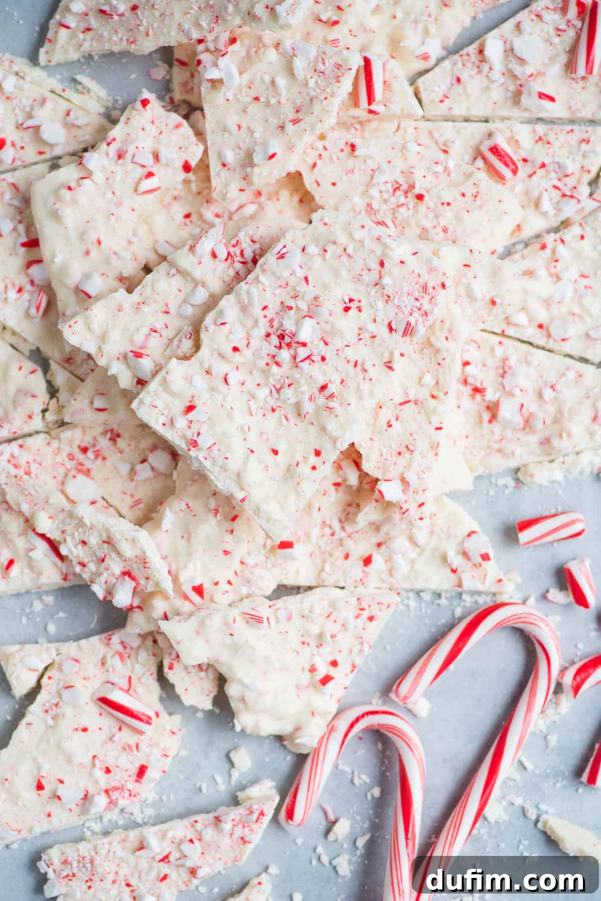 Frosted Peppermint Dream Bark 7 Elegant display of white peppermint bark pieces arranged on a gray surface with whole candy canes and decorative elements.