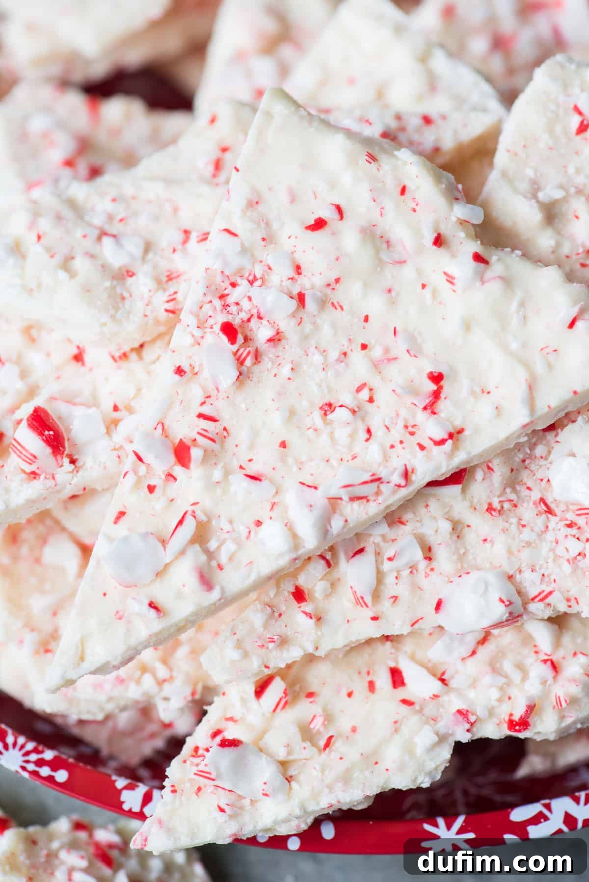 Frosted Peppermint Dream Bark 8 Stack of neatly broken white chocolate peppermint bark pieces on a red Christmas plate, showcasing their inviting texture.