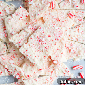 Frosted Peppermint Dream Bark 10 Broken pieces of white chocolate peppermint bark topped with crushed candy canes are scattered on a light surface, creating a festive and textured traditional Christmas dessert.