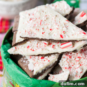 A basket lined with green paper holds pieces of christmas bark, each topped with crushed peppermint candy and a layer of white chocolate.