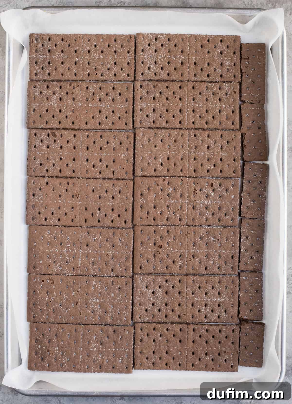 Chocolate graham crackers arranged in a single, neat layer on a baking sheet lined with parchment paper, forming the base for the peppermint bark.