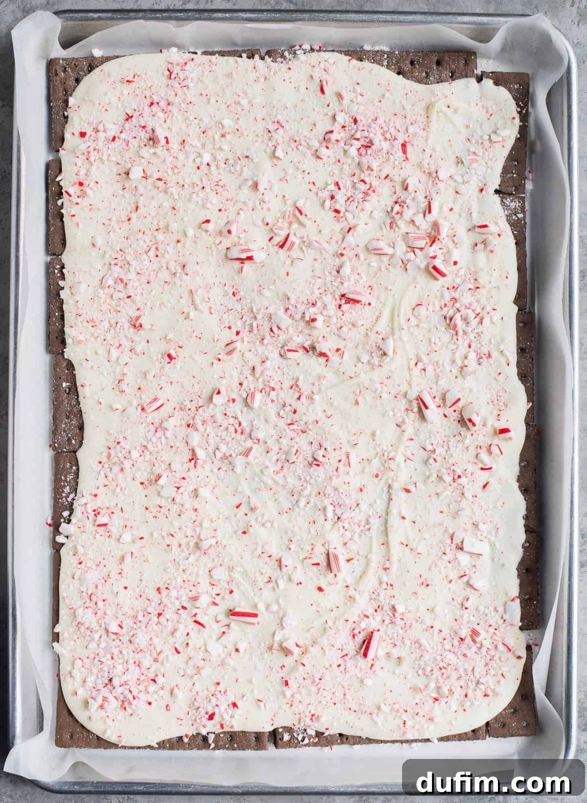 The melted white chocolate layer on chocolate graham crackers now topped with a generous scattering of vibrant red and white crushed candy canes.