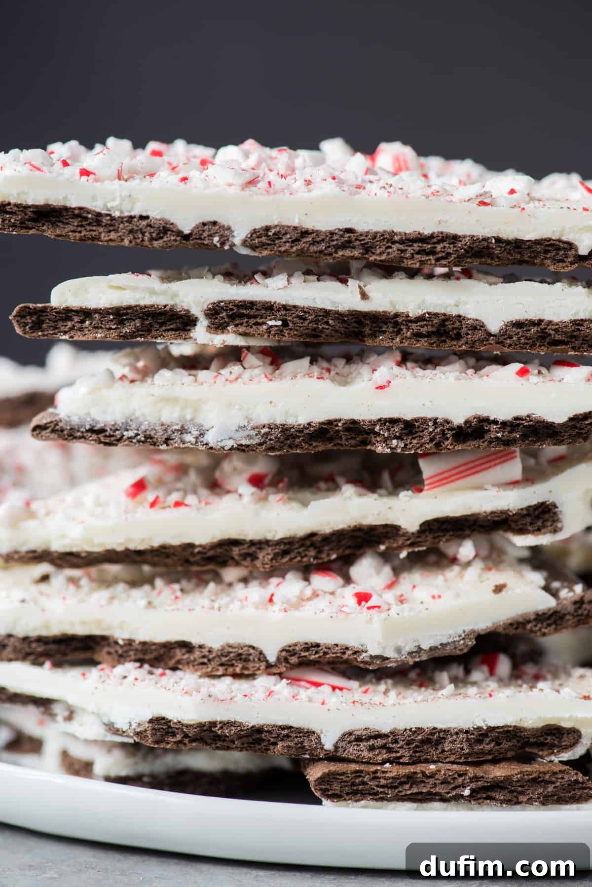 A beautifully stacked pile of finished chocolate peppermint bark pieces, showcasing the multi-layered texture and festive topping.