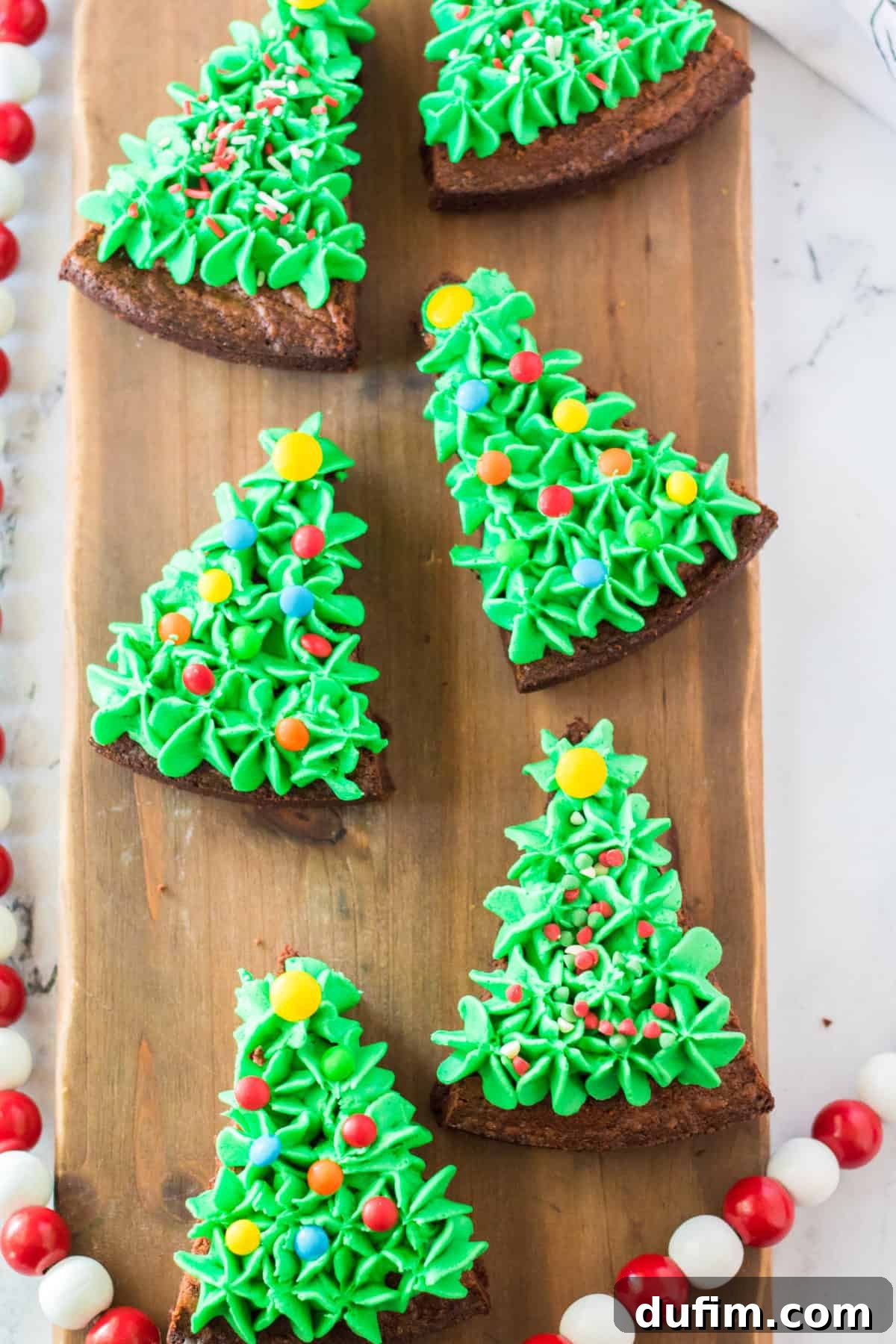brownies cut into triangles and frosted with green frosting and sprinkles to look like Christmas trees on wooden background